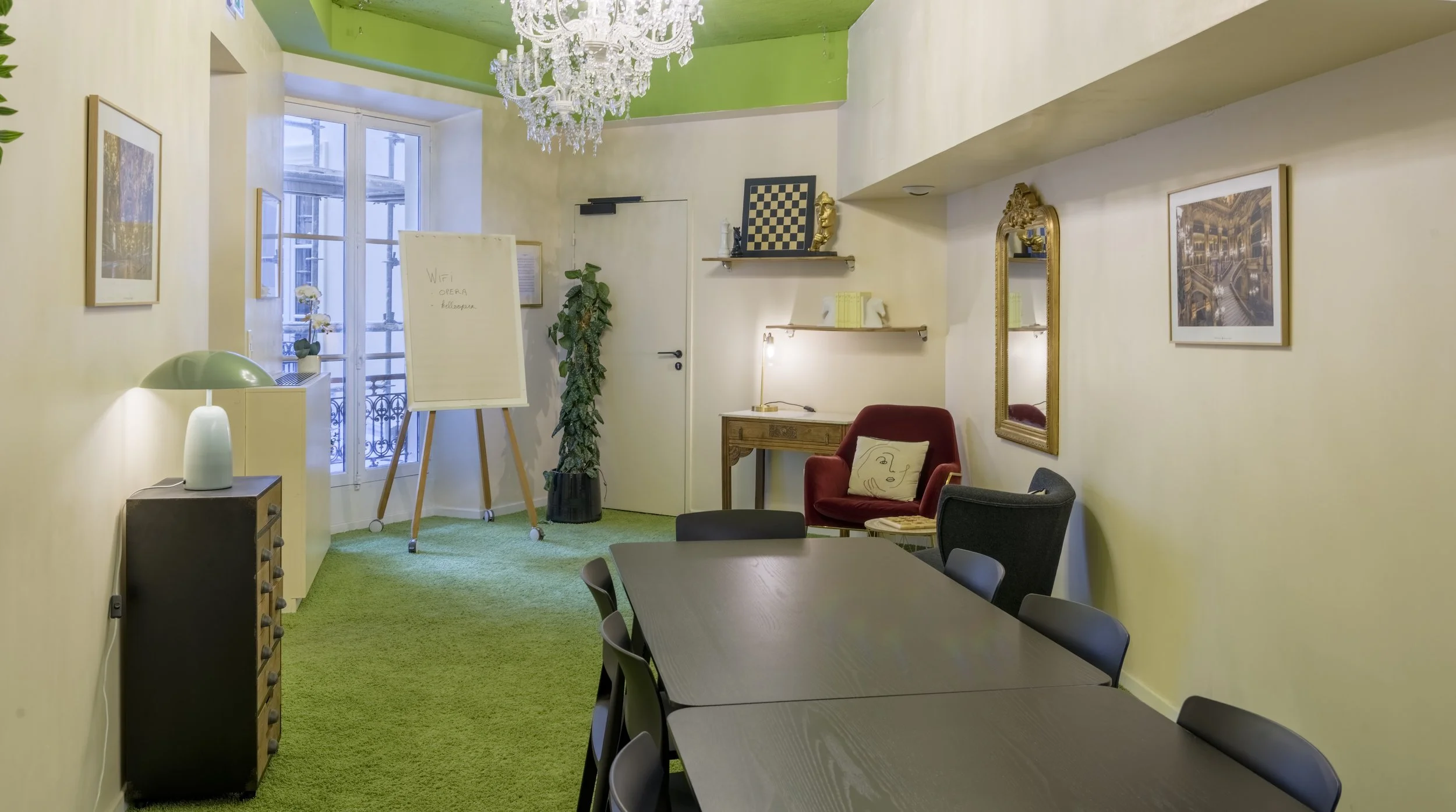 Salle de réunion avec table, chaises, décoration intérieure colorée, fenêtres, œuvres d'art, lampe et plantes.