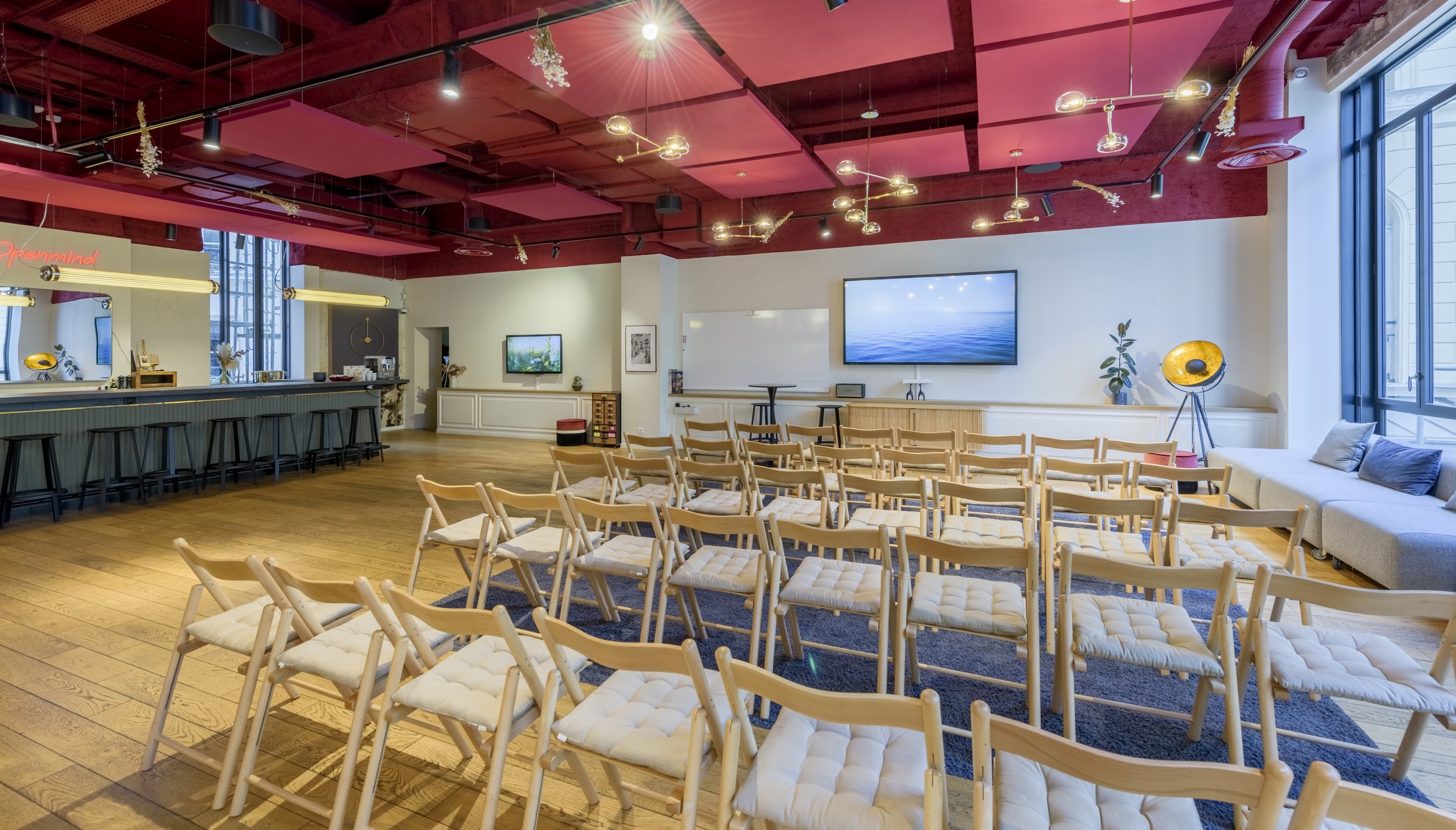 A modern conference room with wooden chairs arranged for a presentation, a large screen on the wall, and a window letting in natural light.