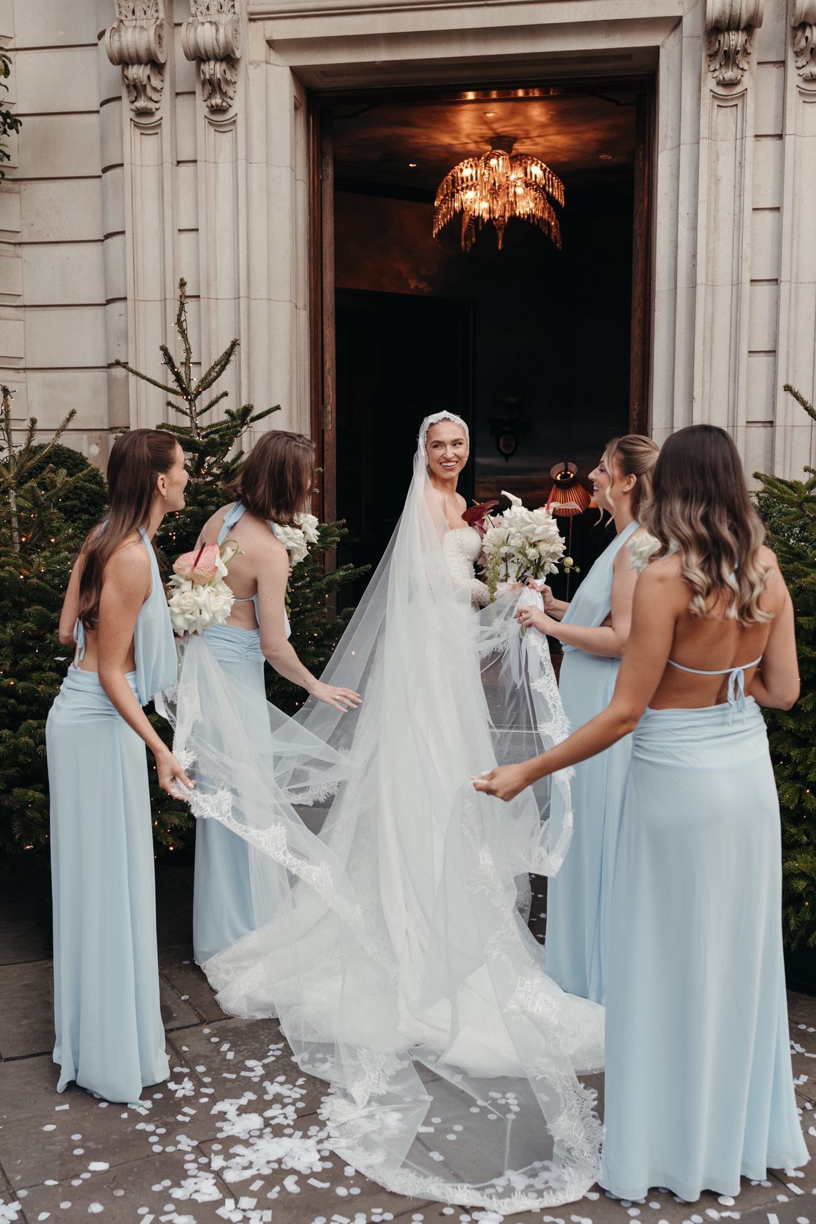 A bride surrounded by her bridesmaids in blue dresses standing outside the NoMad Hotel in London
