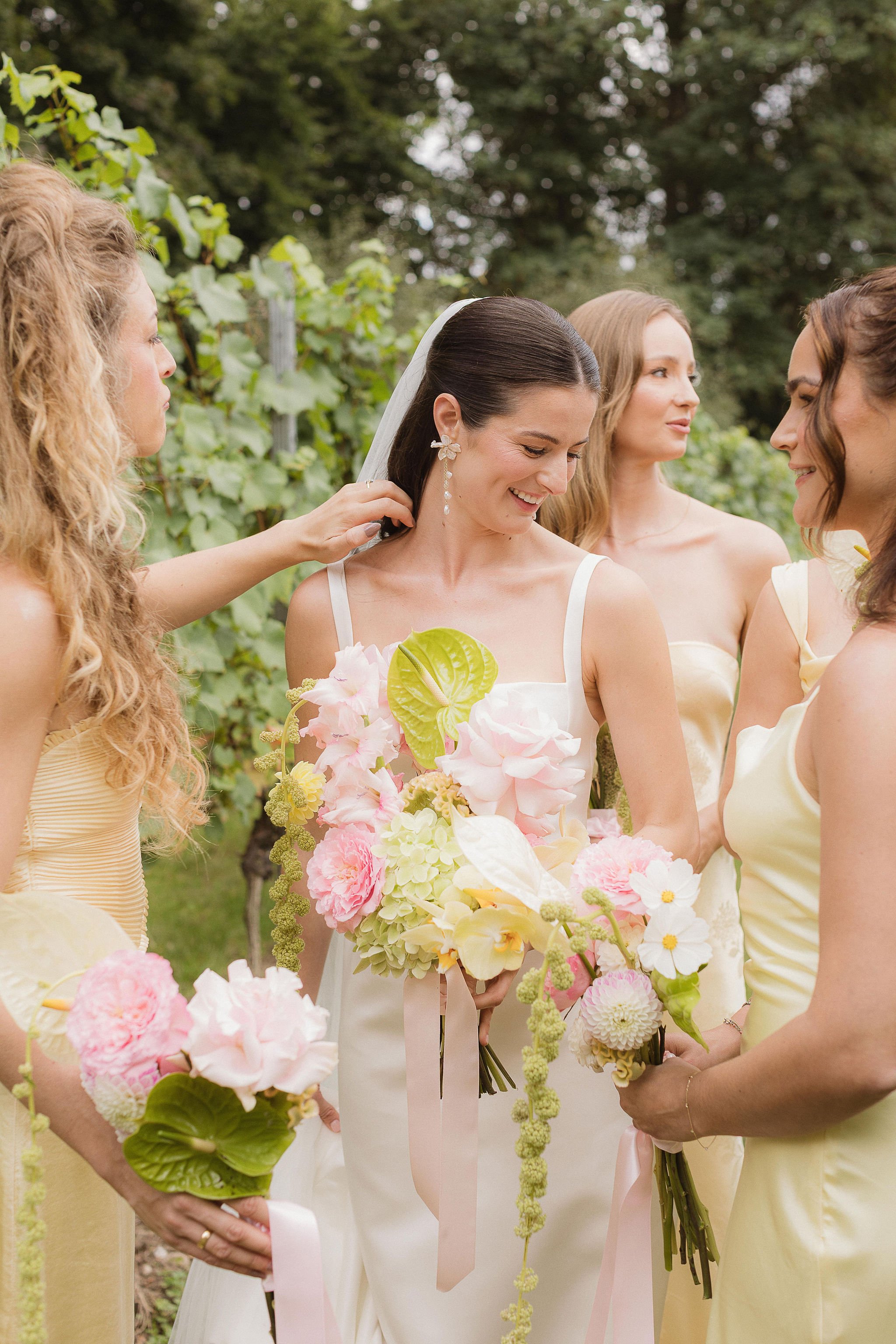 A bride surrounded by her bridesmaids in yellow dresses at the Mount Vineyard in Kent, holding pink, green & yellow modern wedding flowers