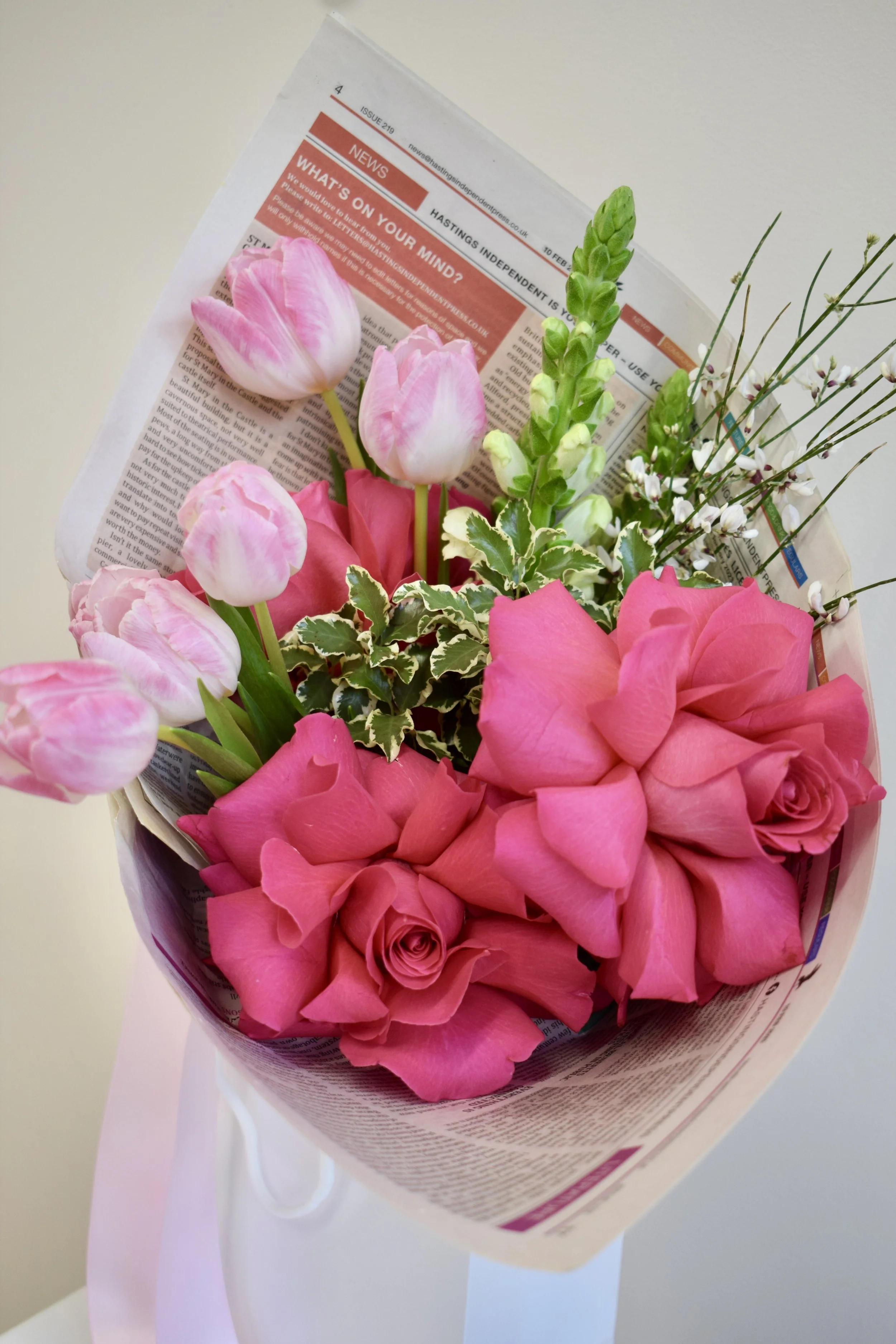 A Valentines Day bouquet full of hot pink reflexed roses, pink tulips, white snapdragons, white ginestra and variegated pittosporum