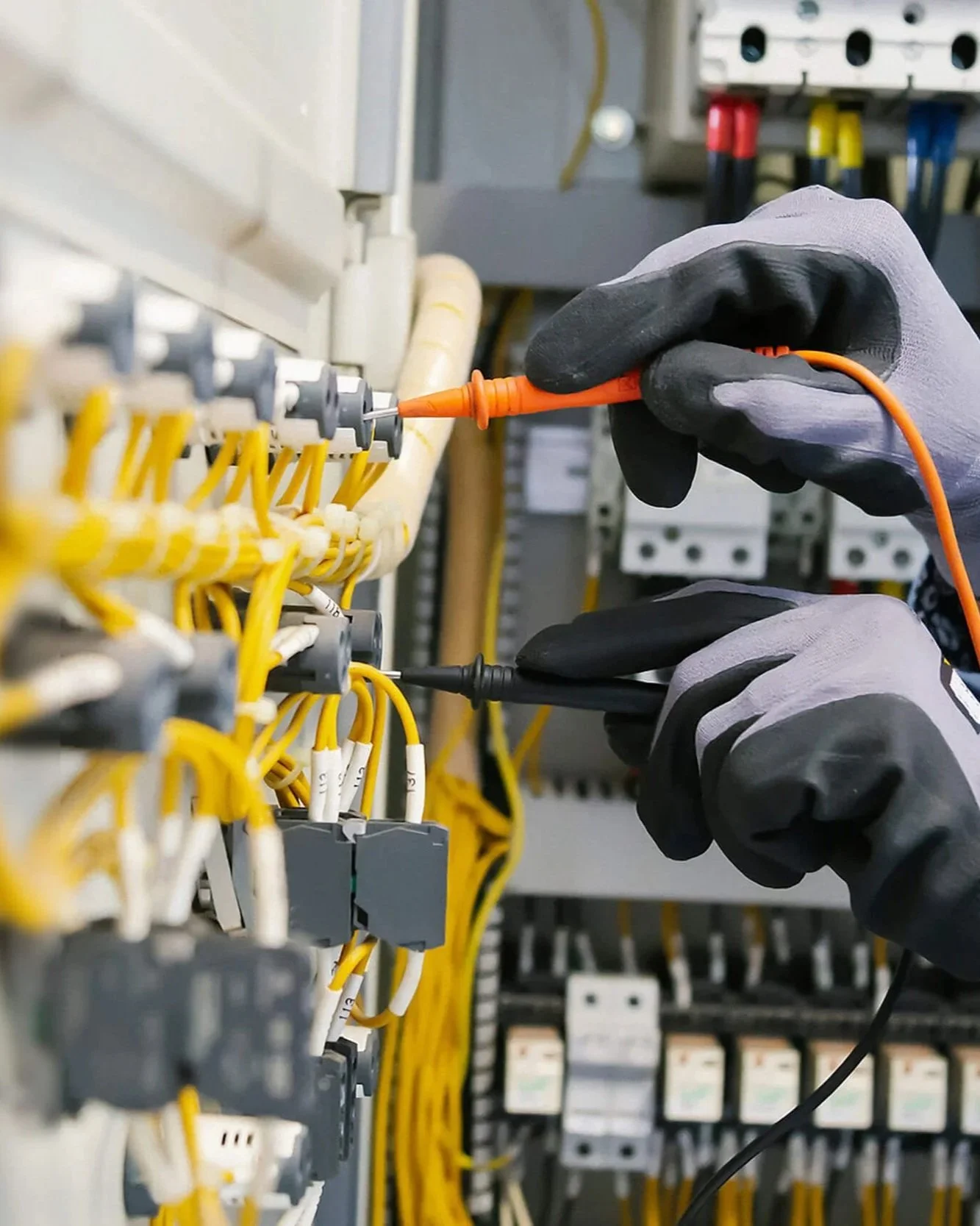 Close-up of a person wearing gloves working with electrical wires using a screwdriver in an electrical control panel.