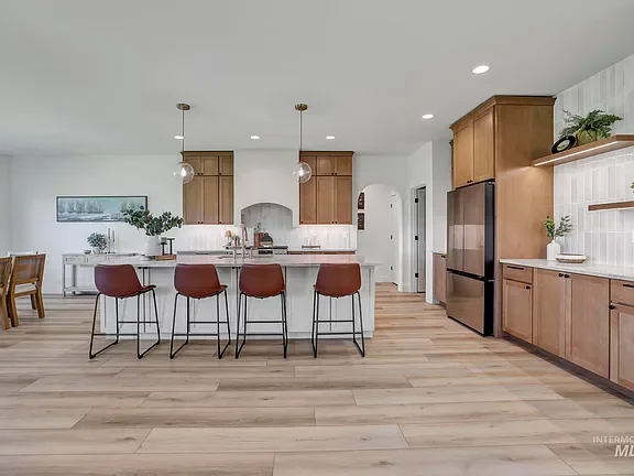Open-concept kitchen and dining area with wooden cabinets, a white island with four red chairs, a stainless steel refrigerator, and minimal decor.