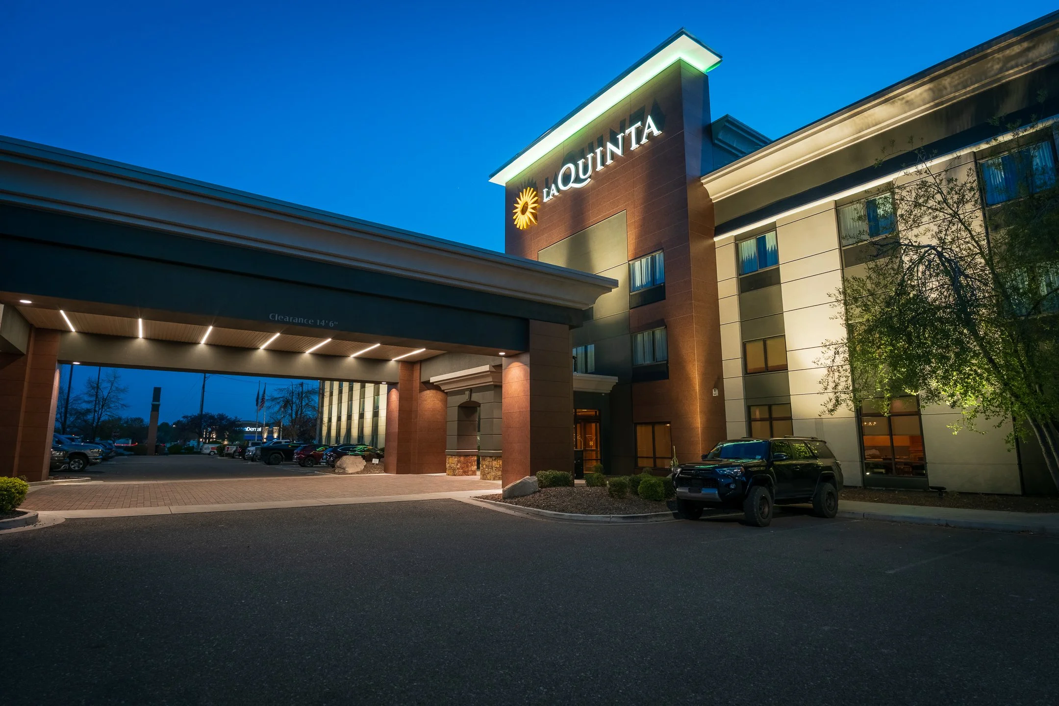 Hotel Taquinta exterior at dusk with parking lot and cars visible.