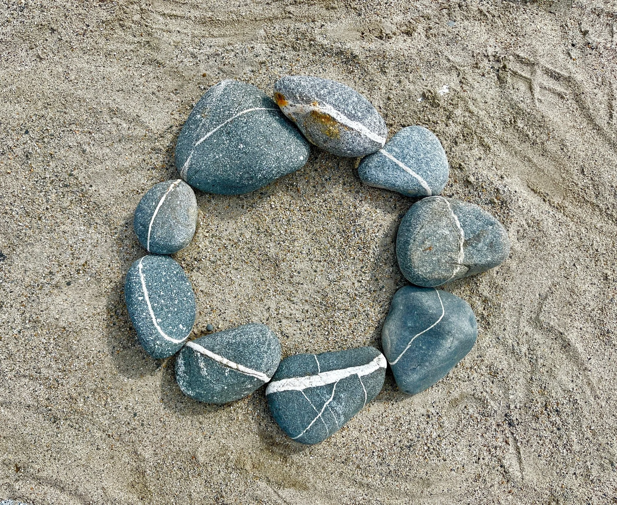 A circle of eight smooth gray stones with white veins arranged on sandy ground.