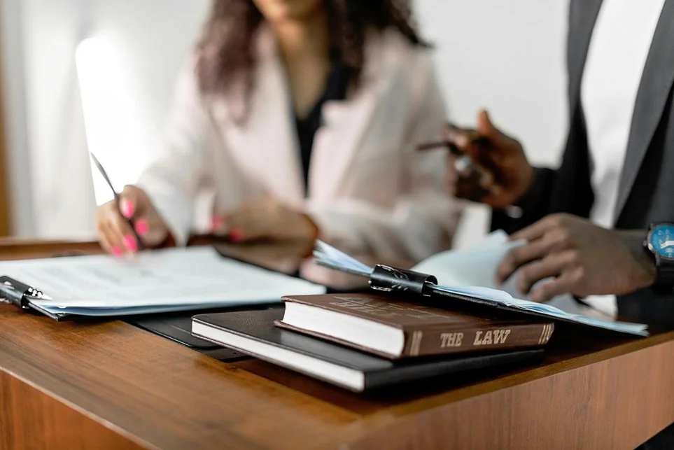 Legal documents and a law book titled 'The Law' on a wooden table during a discussion between two professionals.
