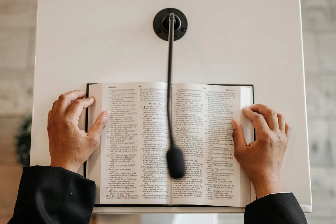 Hands holding an open book on a lectern with a microphone in front of the book.