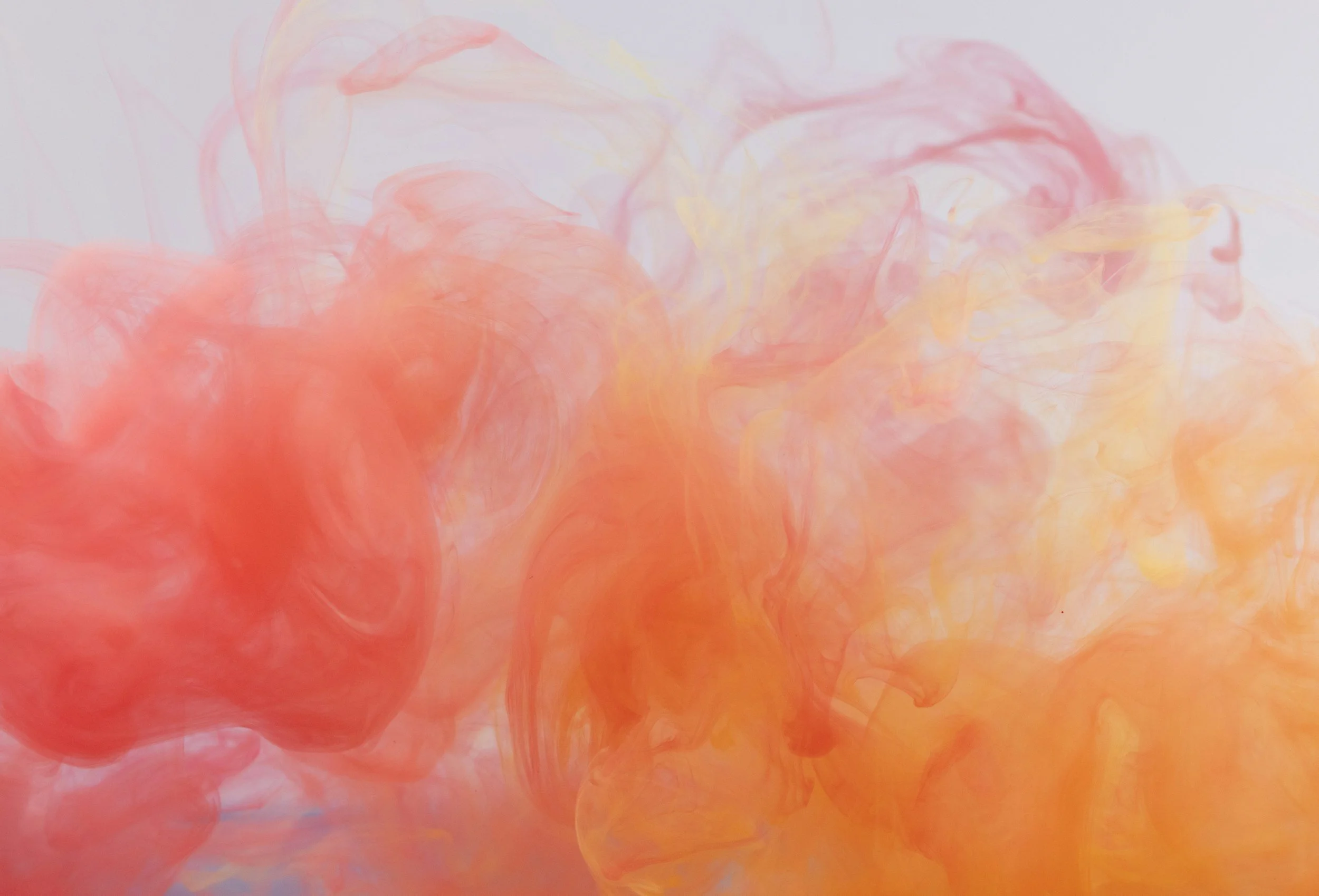 Swirling orange, yellow, and pink ink in water creating abstract patterns.