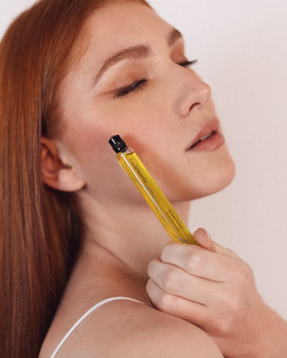 A woman with closed eyes and long red hair holds a yellow perfume bottle near her face.