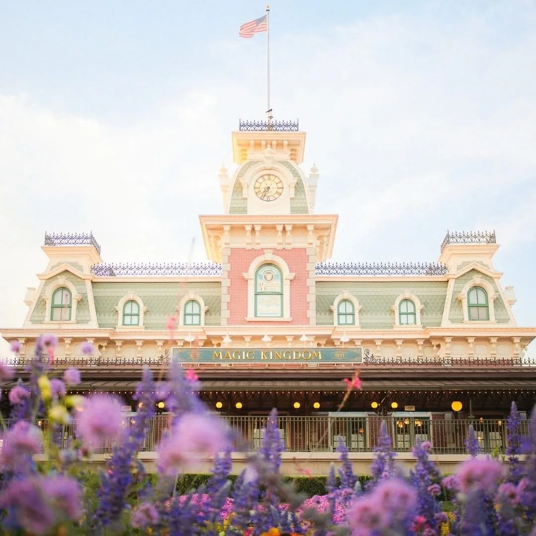 Front view of Disneyland's Magic Kingdom entrance with colorful flowers in the foreground and a clear sky.