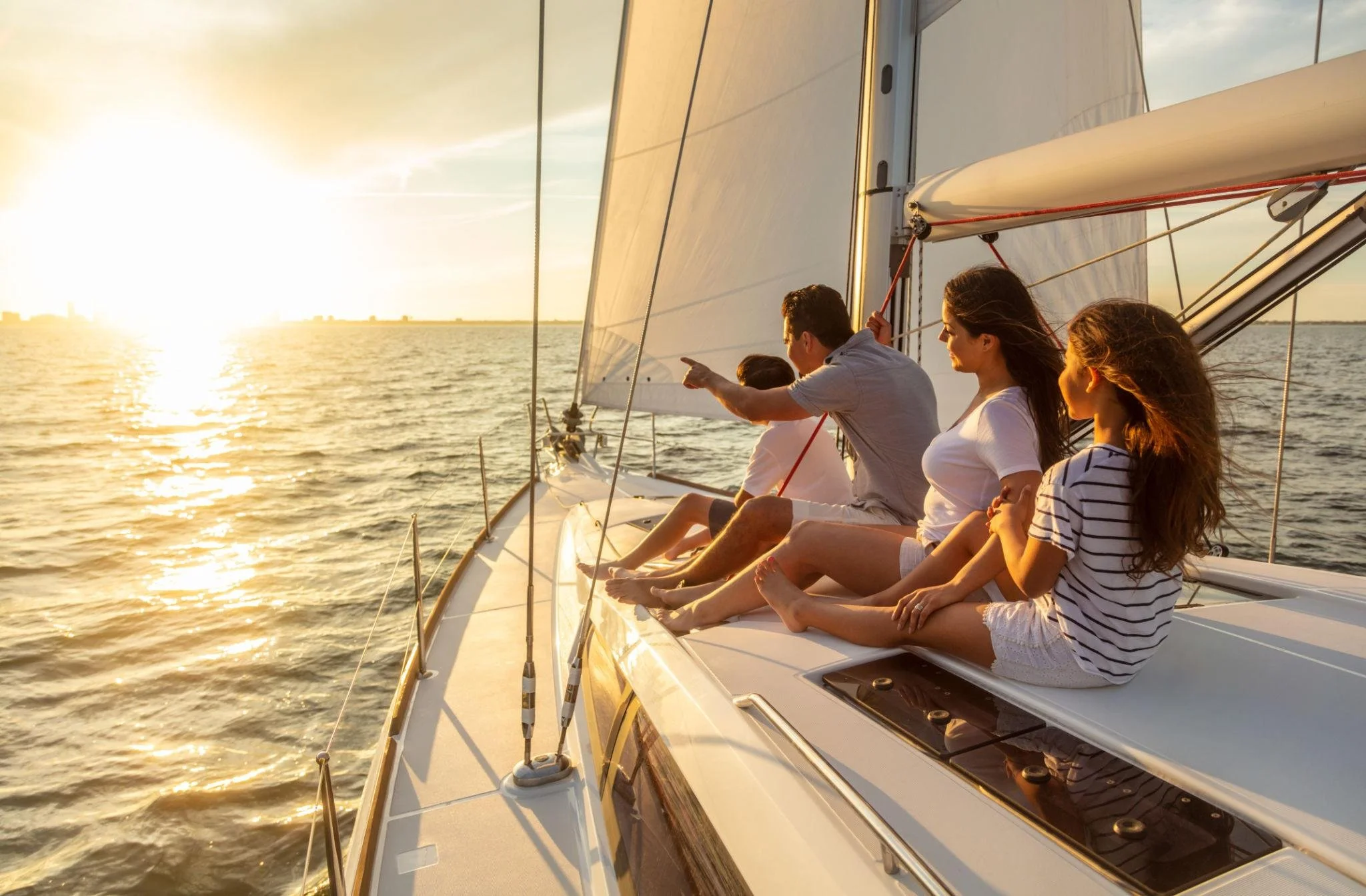 A group of people sitting on a sailboat during sunset, looking out over the water.