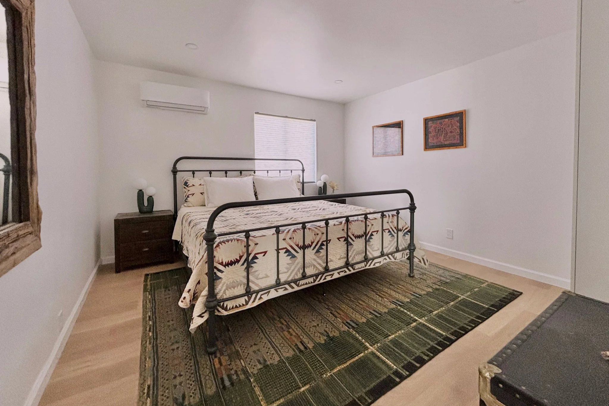 Bedroom with a metal bed frame, patterned bedding, nightstand, lamp, and framed artwork on the white wall.