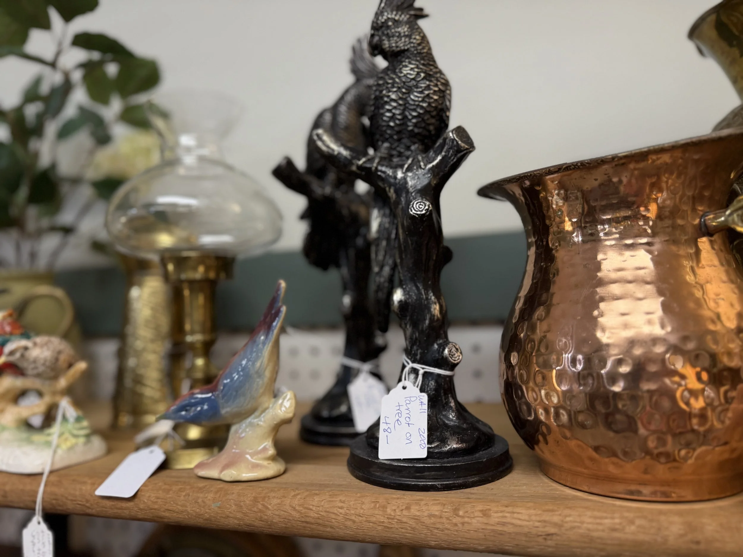 Various decorative items on a wooden shelf, including a black bird figurine on a tree branch, a copper hammered vase, and a ceramic bird sculpture.