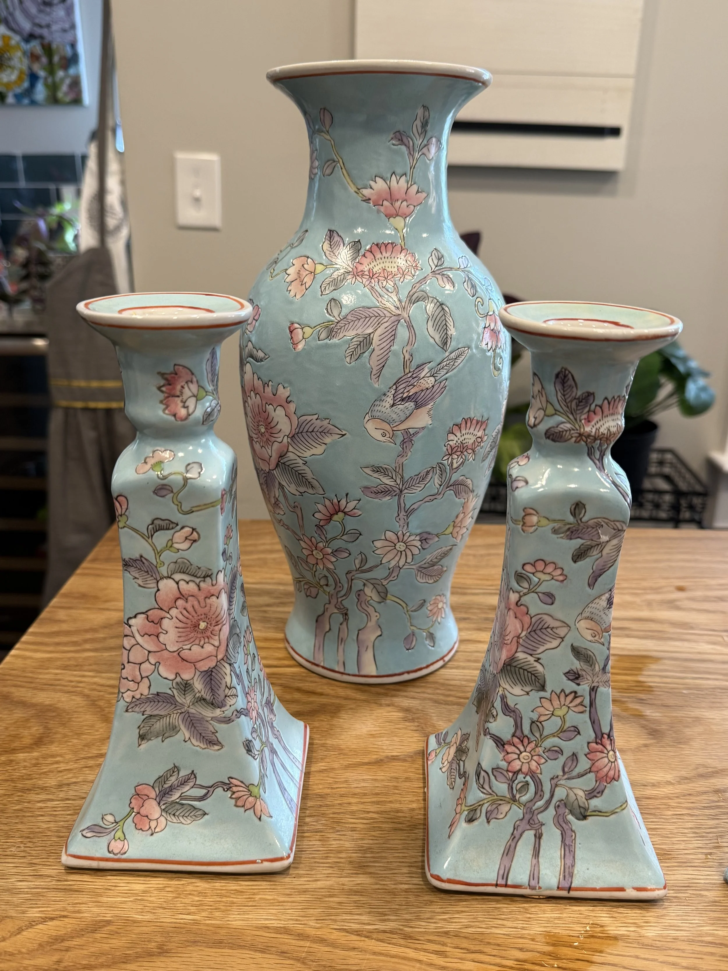 A set of three ceramic vases with a light blue background and pink floral and bird designs, placed on a wooden surface.