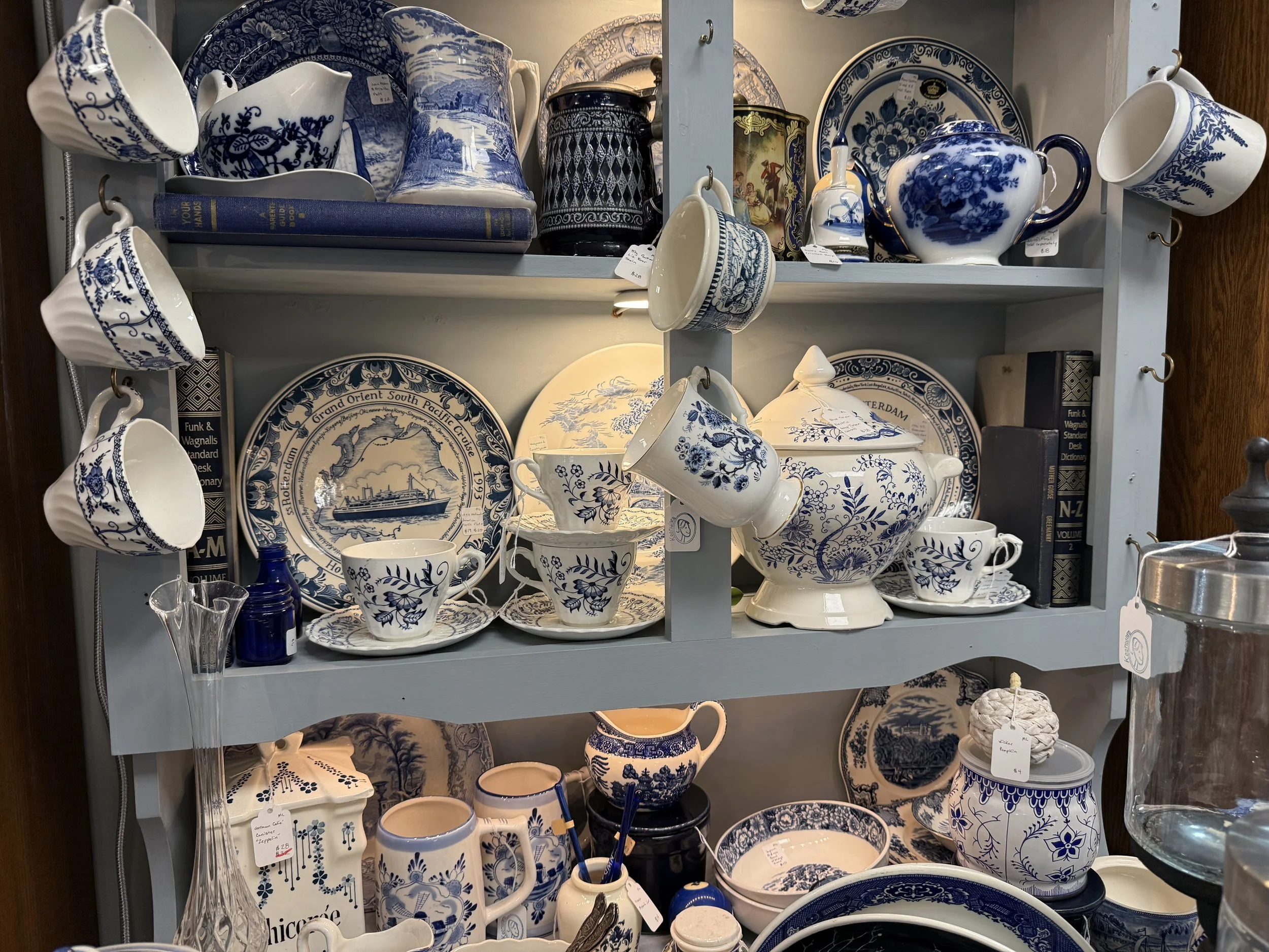 A display shelf filled with blue and white ceramic dishes, cups, teapots, and decorative items with intricate patterns.