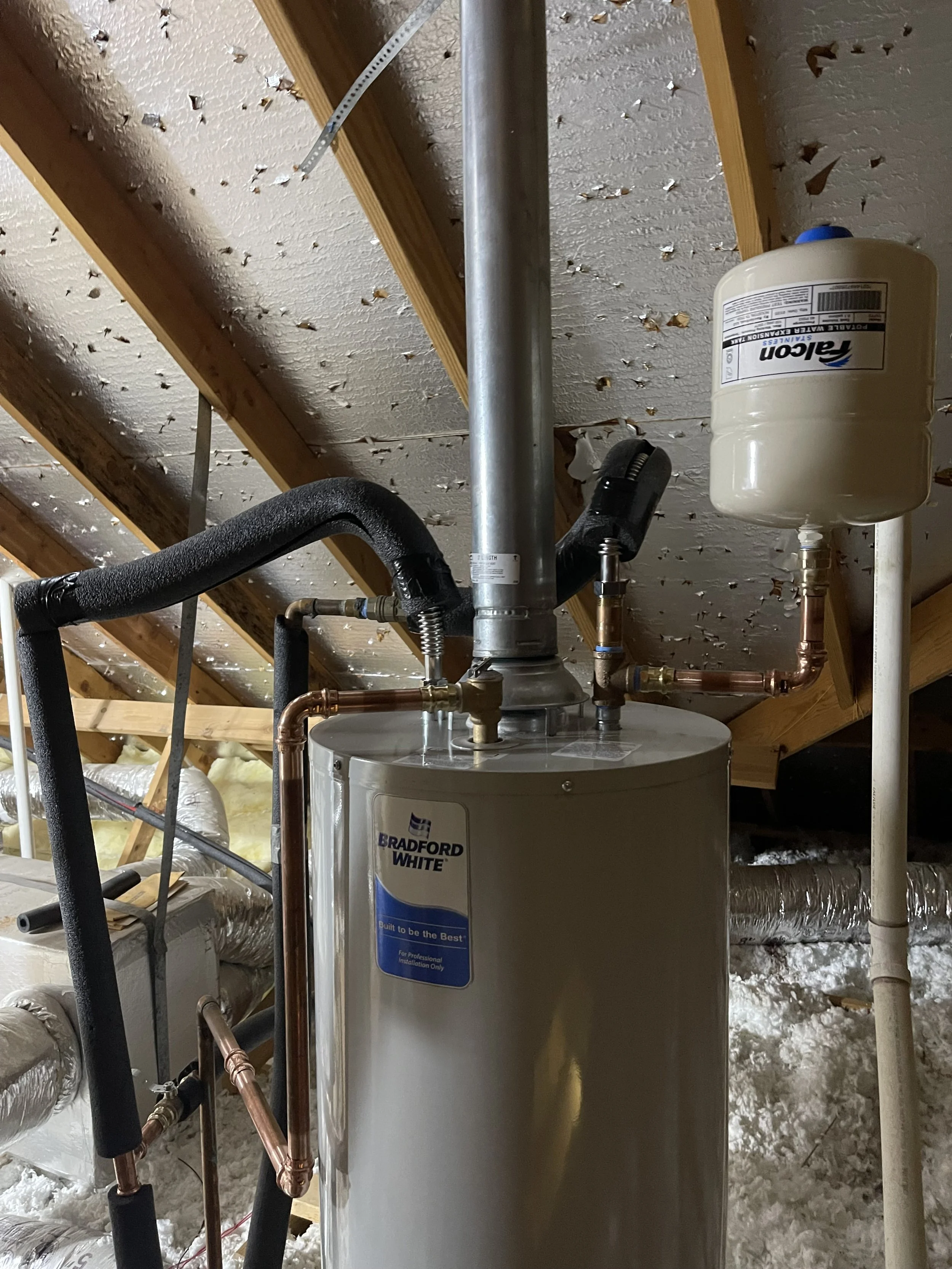Water heater in an attic space with pipes and insulation around.