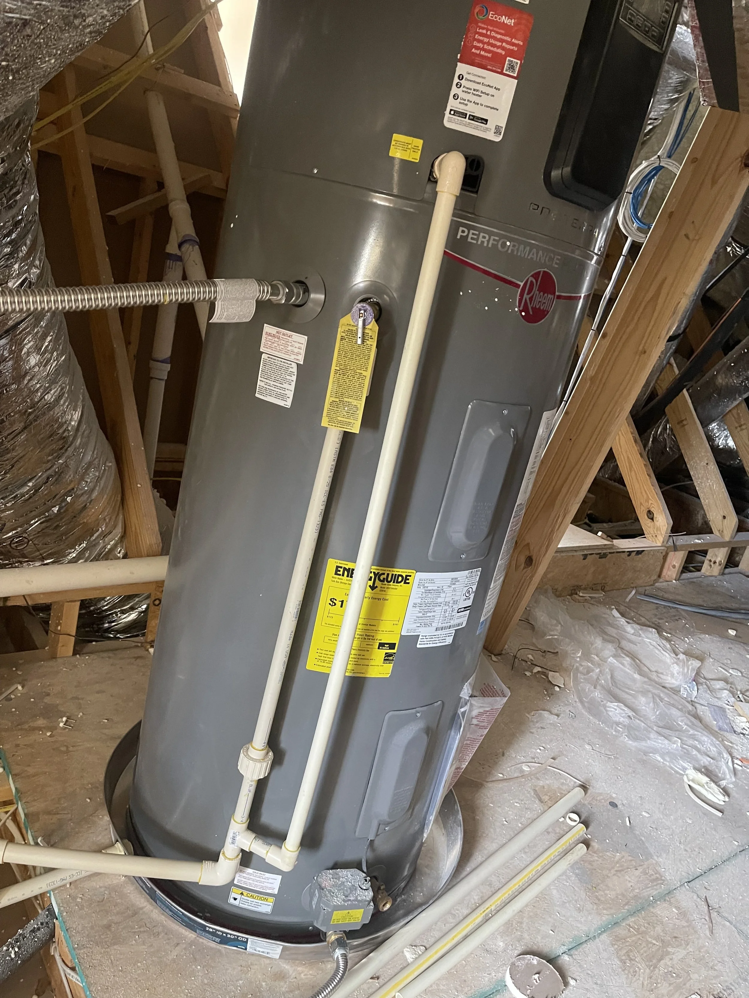 A water heater in an attic with construction materials and exposed wooden framing.