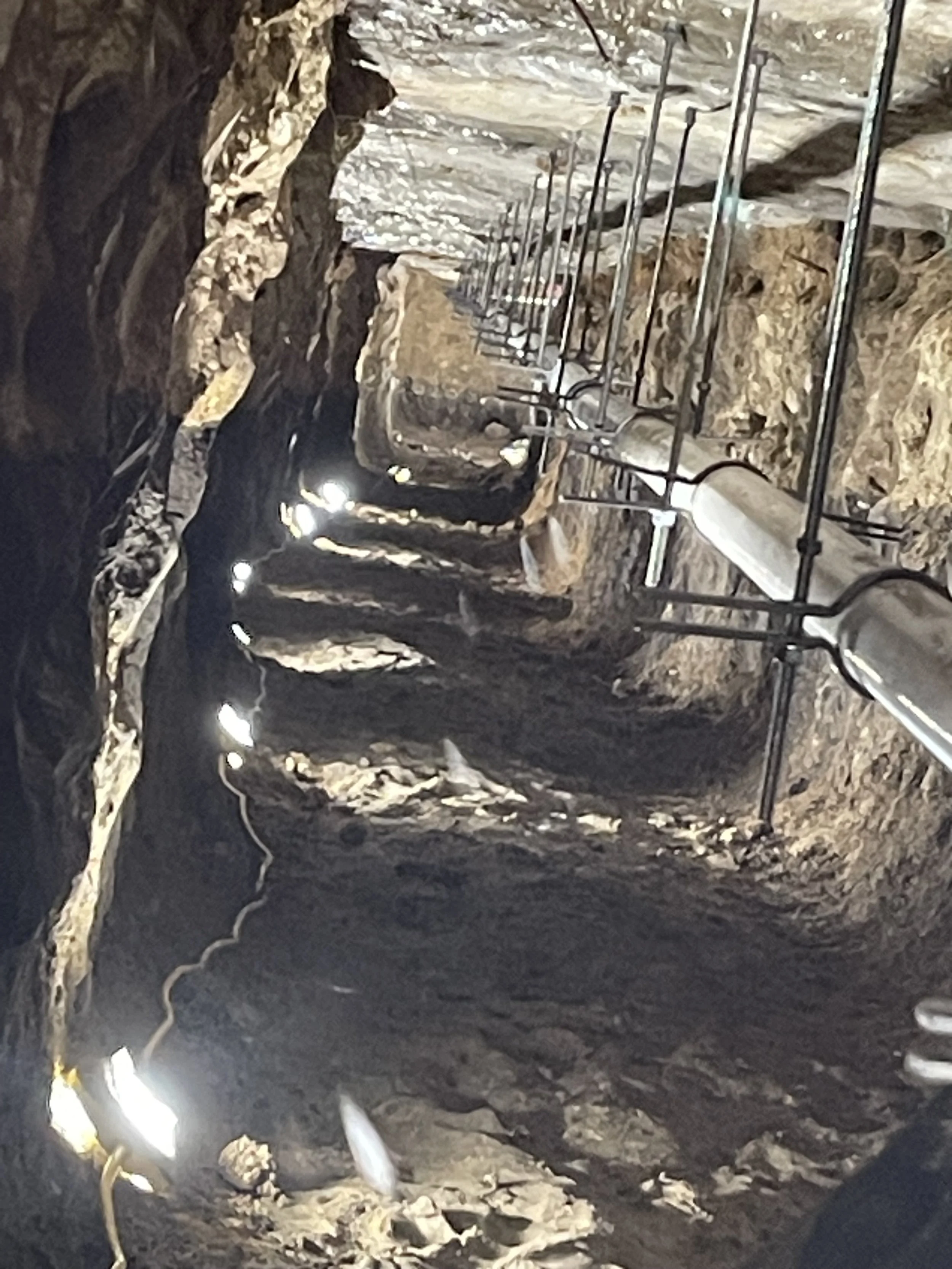 Inside a deep underground mine with a ladder and railings along the rocky walls.