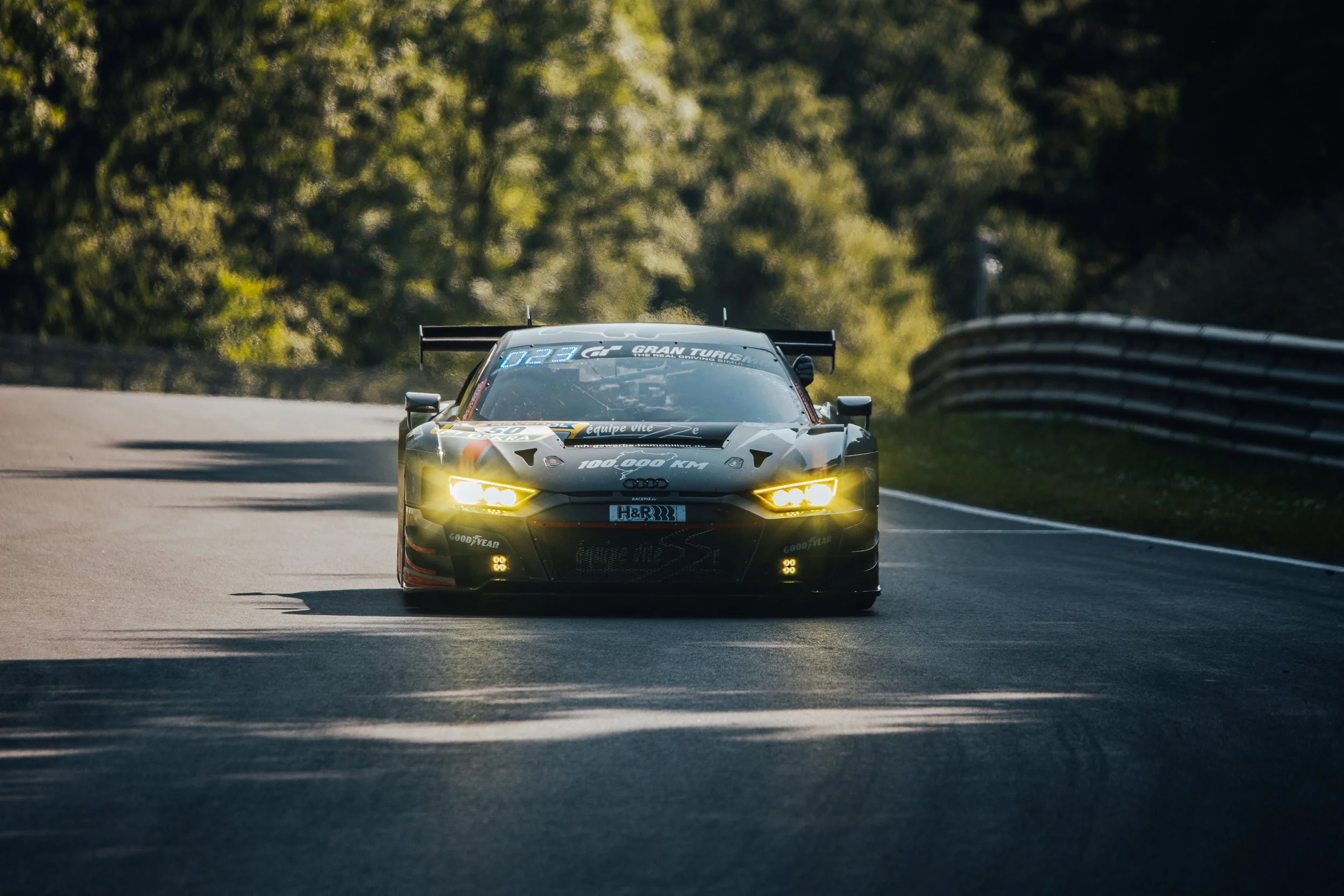 A black racing car with yellow headlights driving on a winding road surrounded by trees.