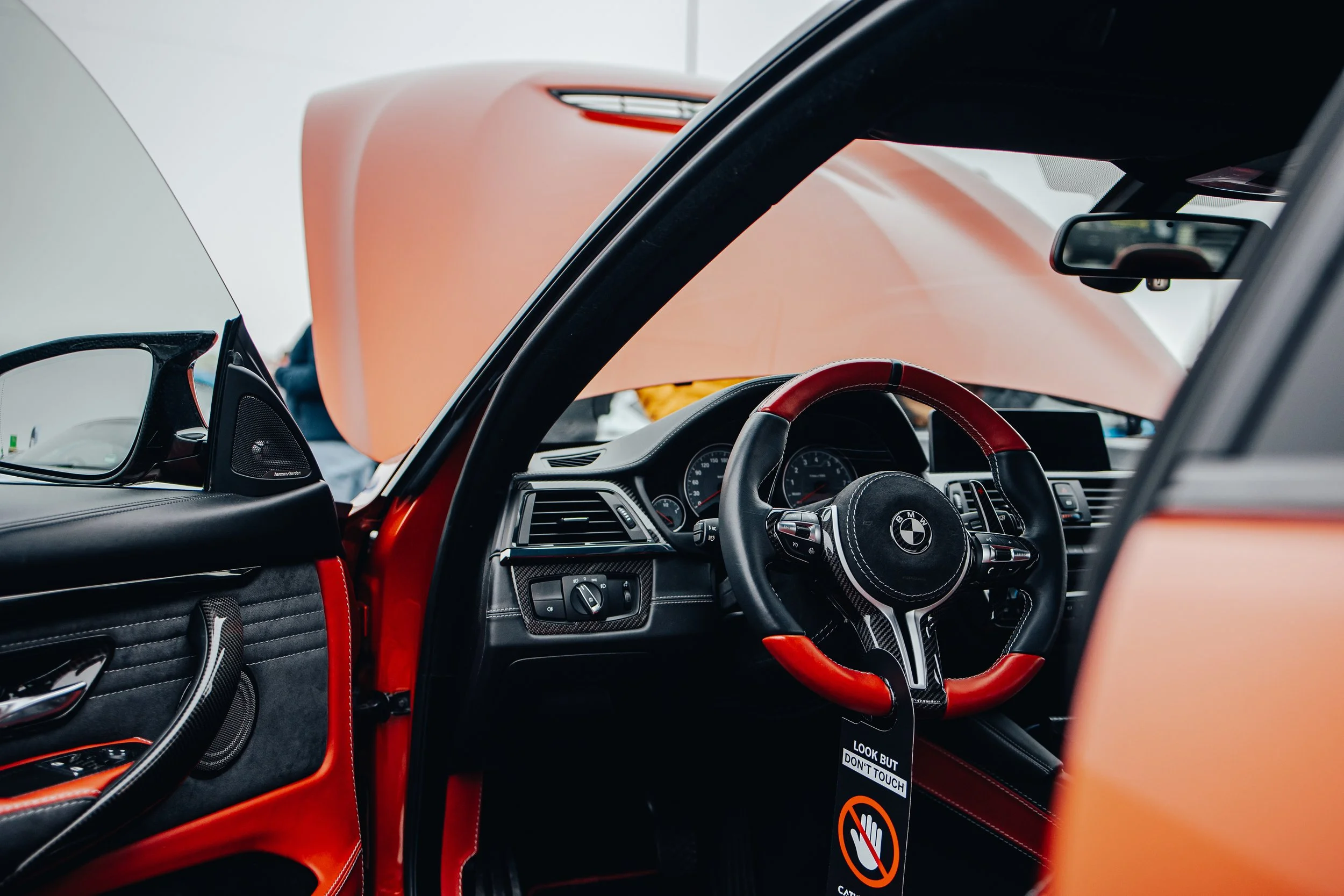 Close-up view of the interior of a BMW car, showing the steering wheel with BMW logo, dashboard, and the hood of the car being lifted.
