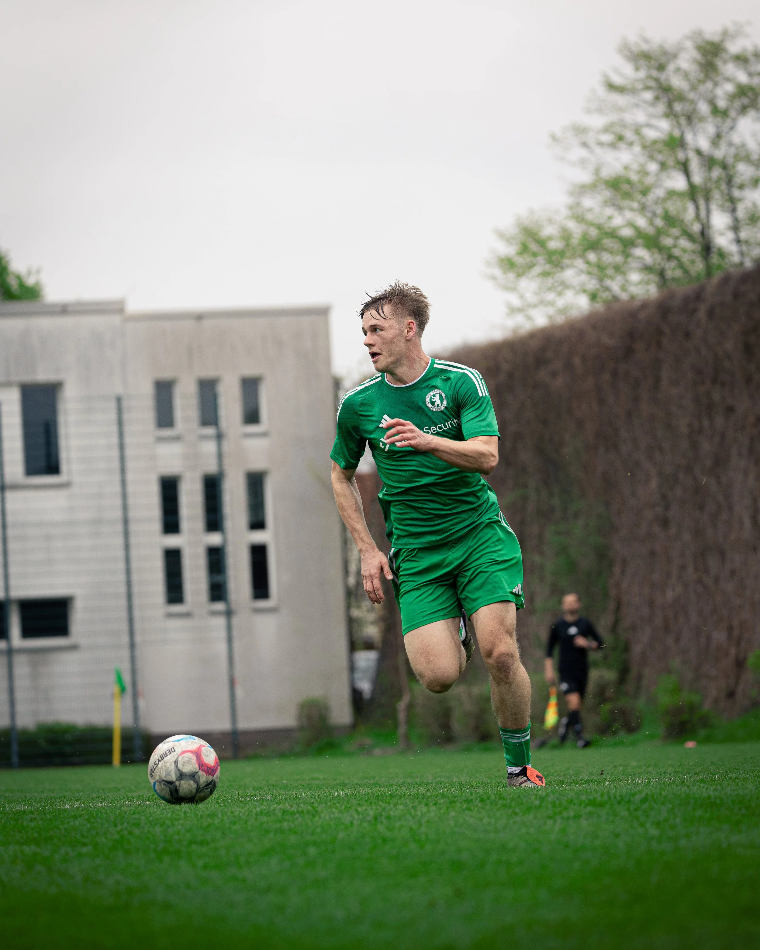 A soccer player in a green uniform running on the field towards the ball during a game.
