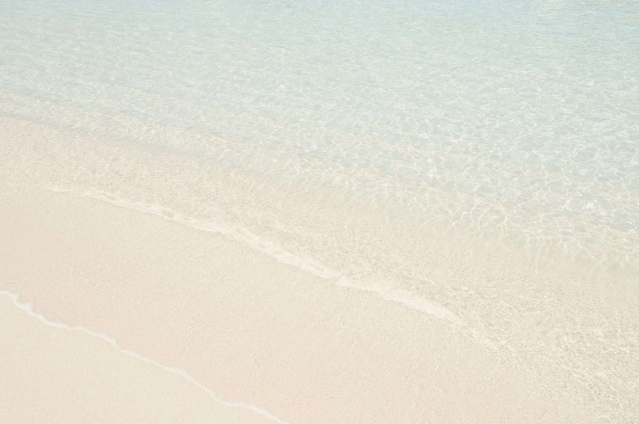 A peaceful beach scene with clear, shallow water and white sand.