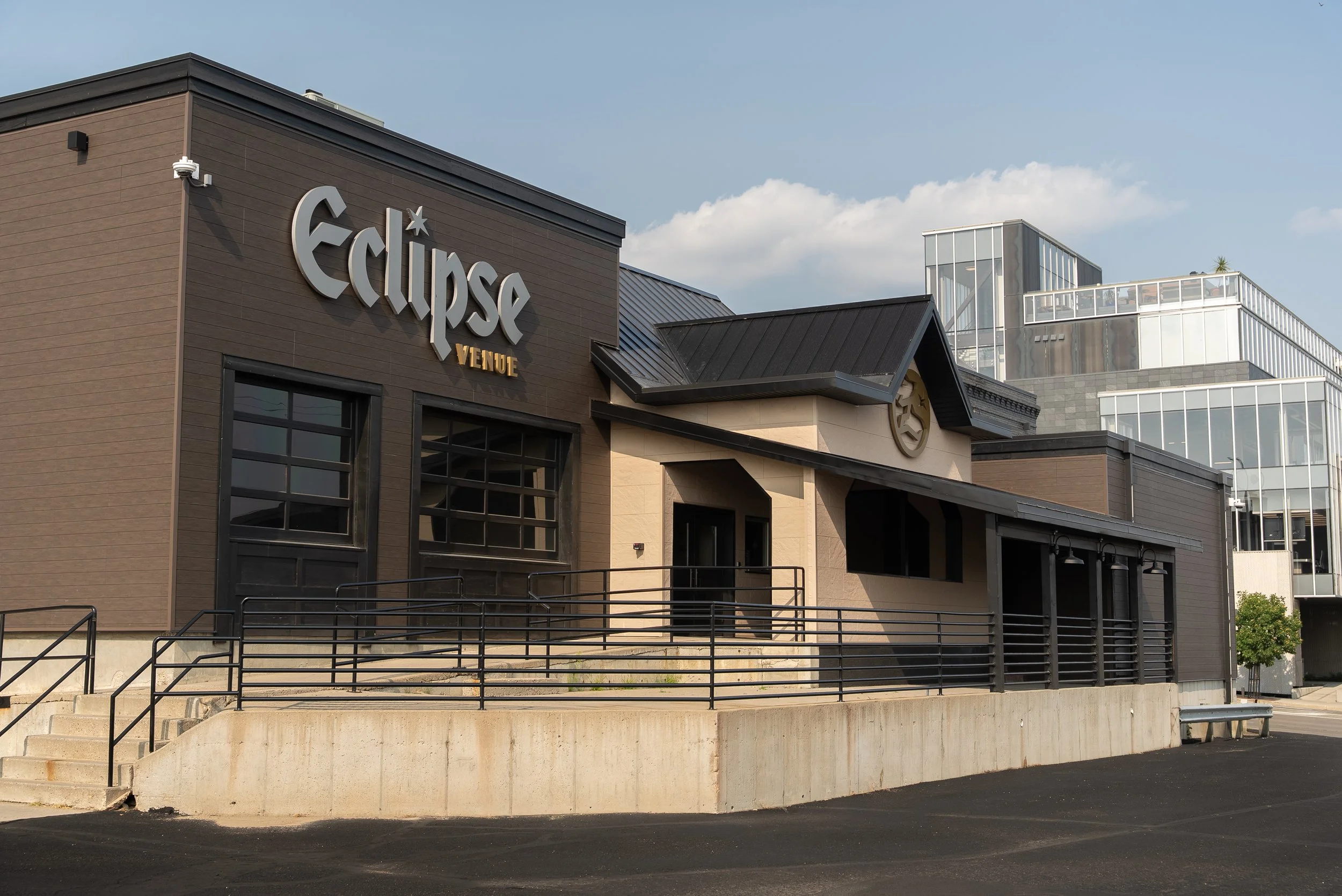 Exterior of the Eclipse Venue building with modern architecture, large sign, stairs, and ramp leading to the entrance, against a partly cloudy sky.