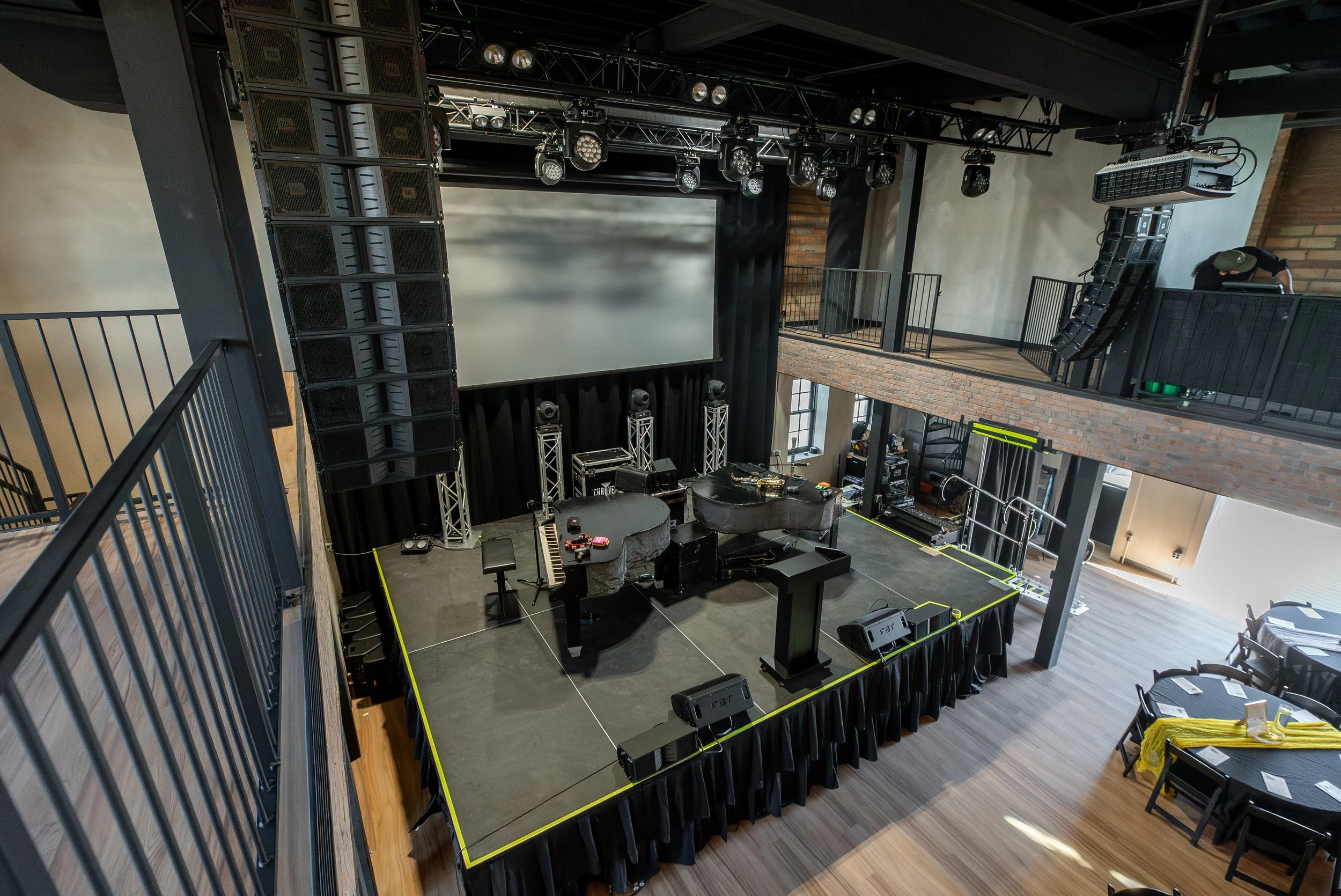 Empty stage with a large projection screen, two grand pianos, and various sound equipment in a modern venue.
