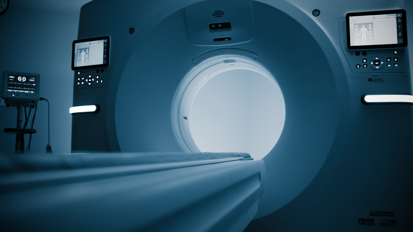 Inside an MRI scanner room showing the circular bore of the MRI machine and medical monitors with patient information.