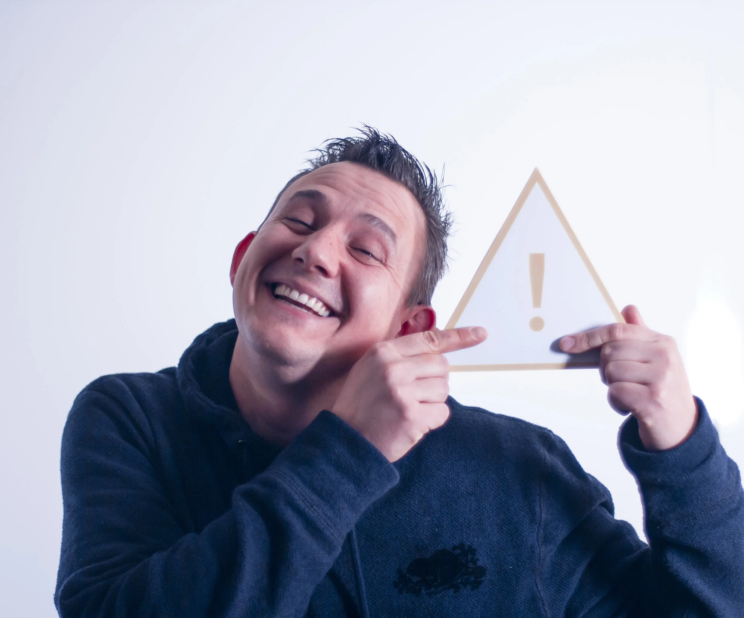 A man with a big smile, pointing to a triangular sign with an exclamation mark on it.