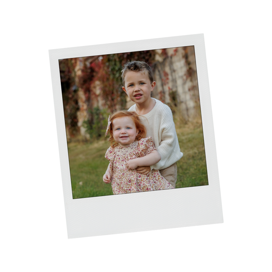 A young boy and a little girl standing outdoors in autumn, smiling and looking at the camera.