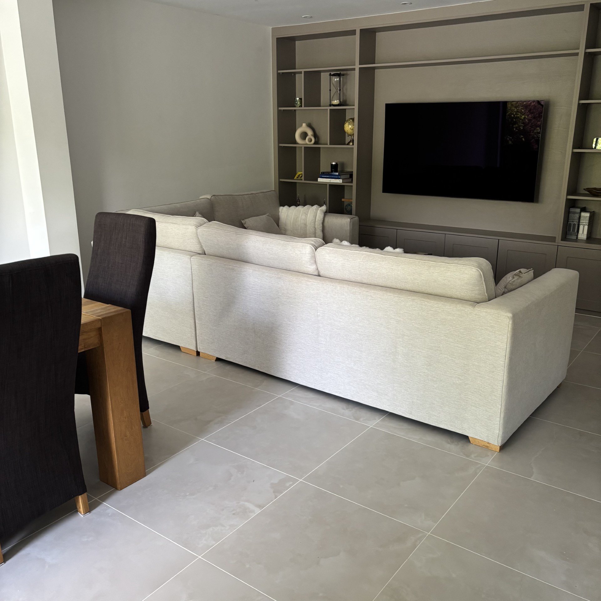 Large format grey marble-effect porcelain floor tiles in a modern living room with media wall and corner sofa