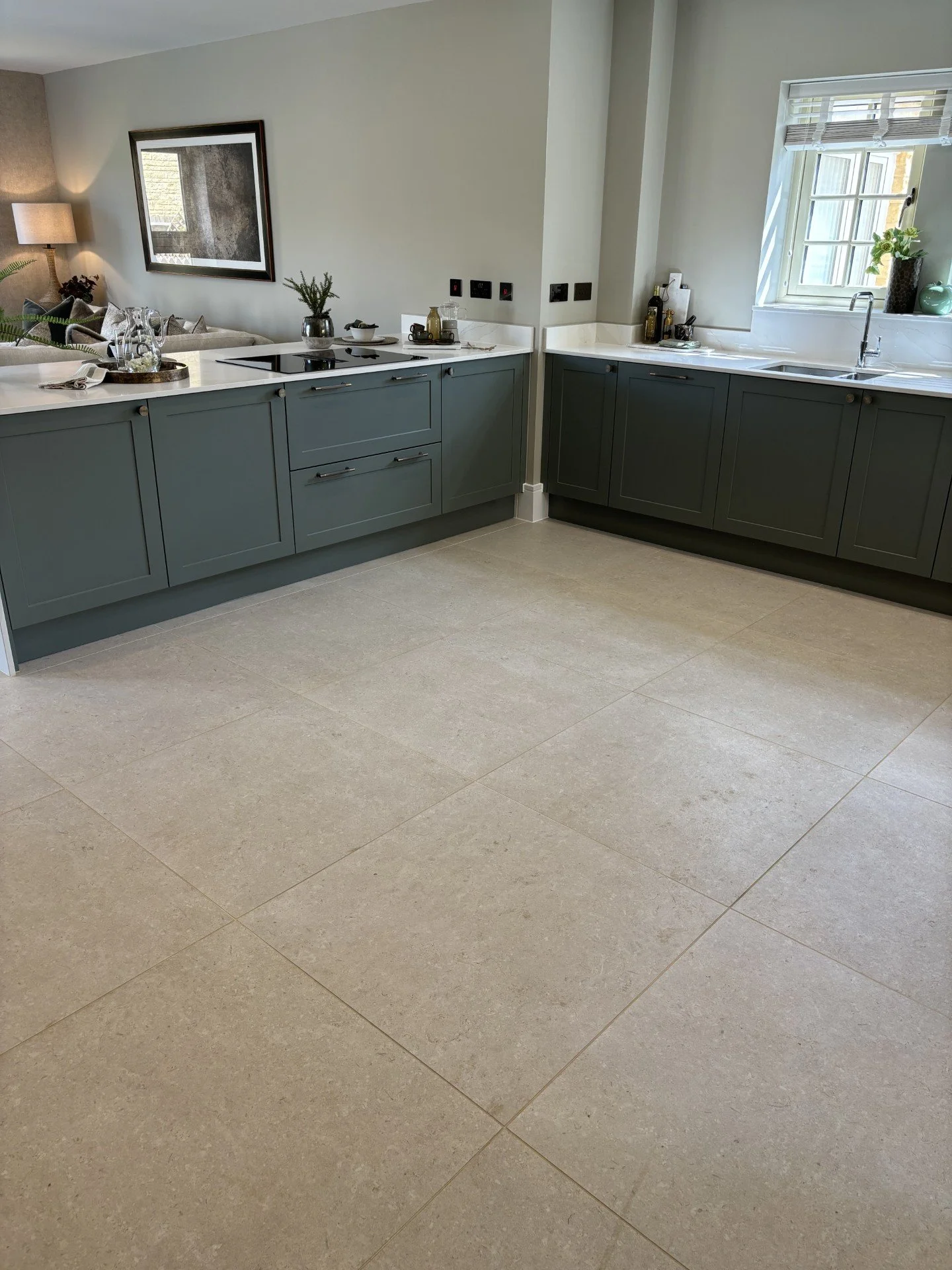 Cream limestone-effect porcelain floor tiles in a kitchen with green shaker cabinets and white worktops