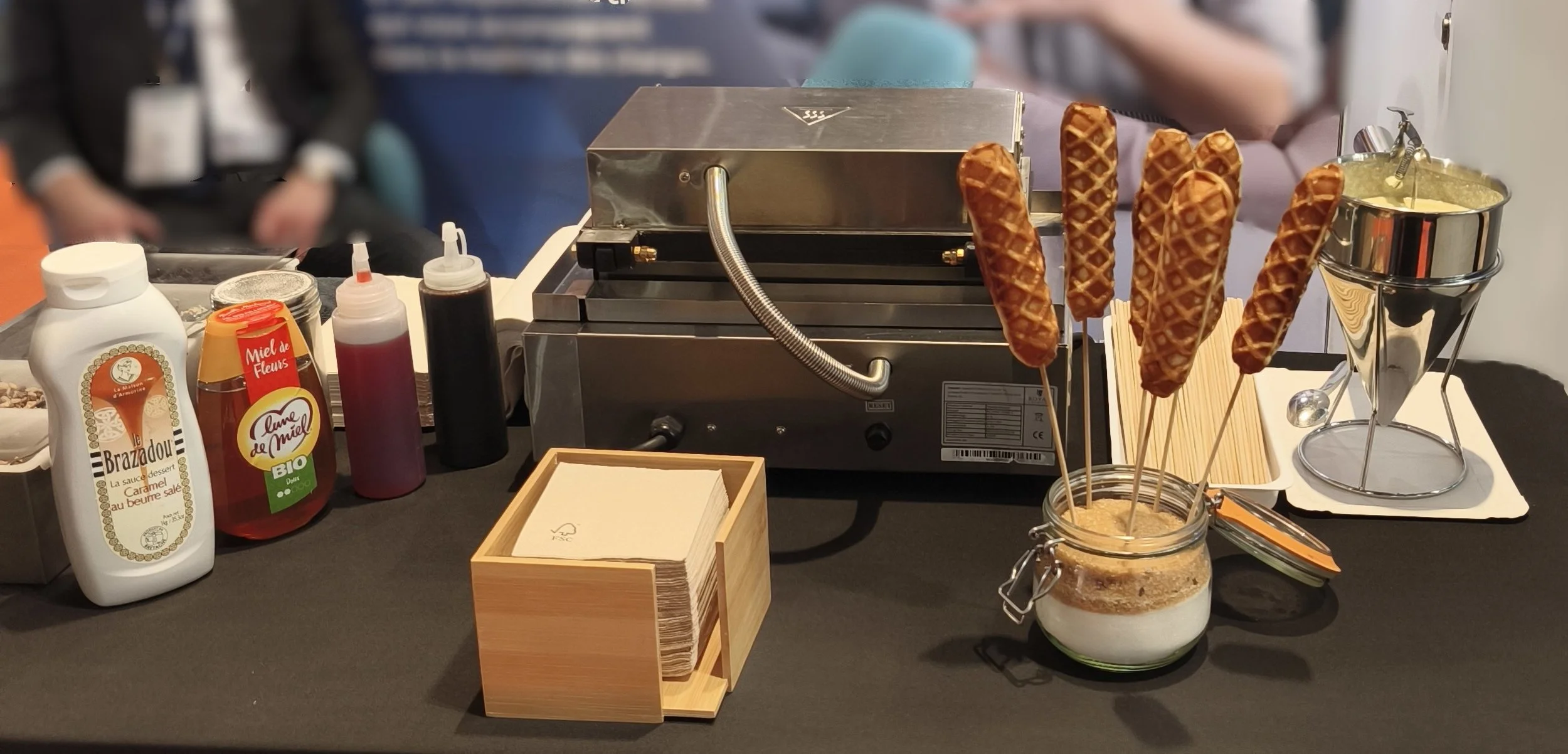 Gaufrier avec cônes de gaufre à l'appareil, cuve avec mix pour ice cream, bouteilles de sirop, miel, nappe à serviettes en papier, ingrédients de artisanat pour crêpes ou gaufres.
