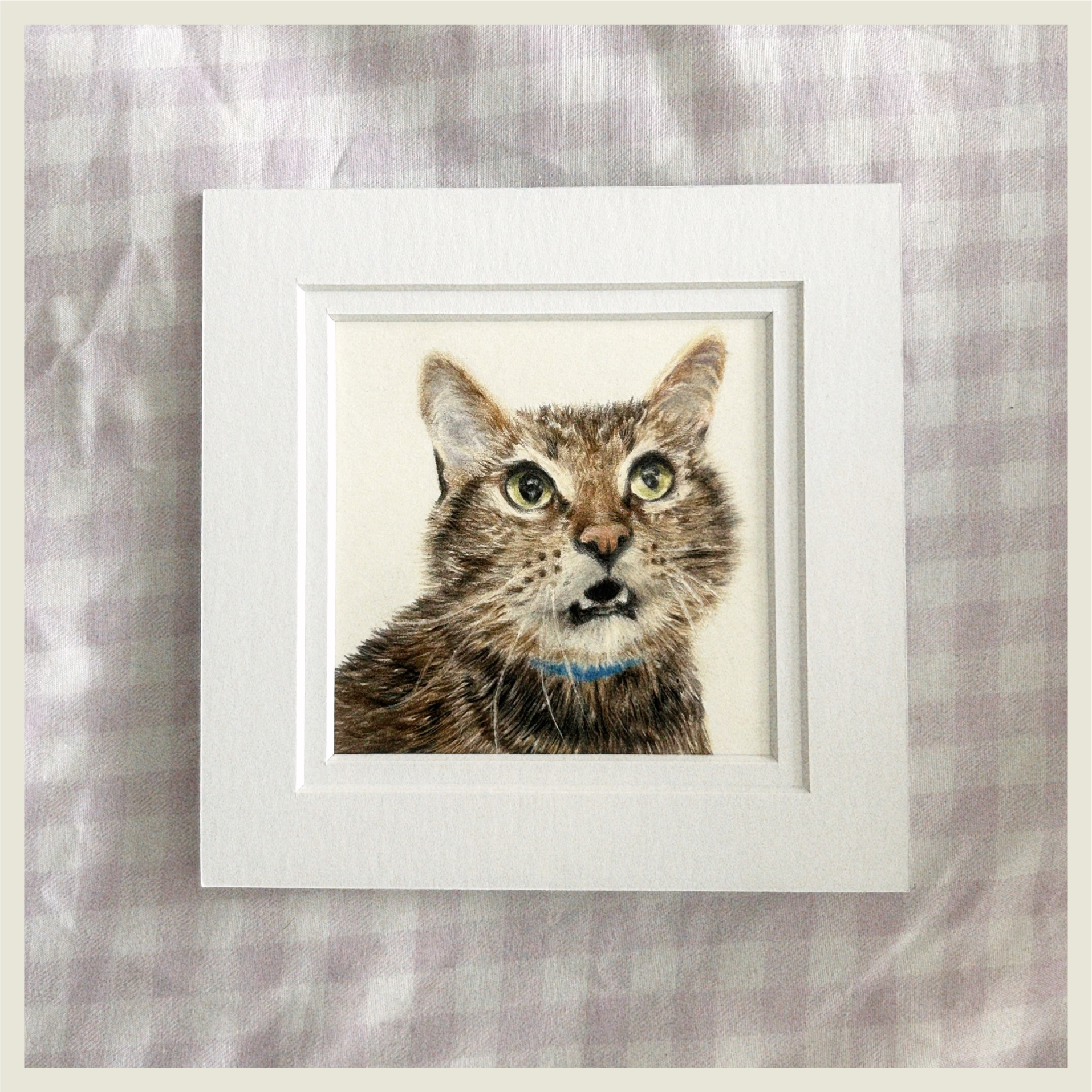 A framed artwork of a realistic realistic painting or drawing of a tabby cat with green eyes, wearing a blue collar.