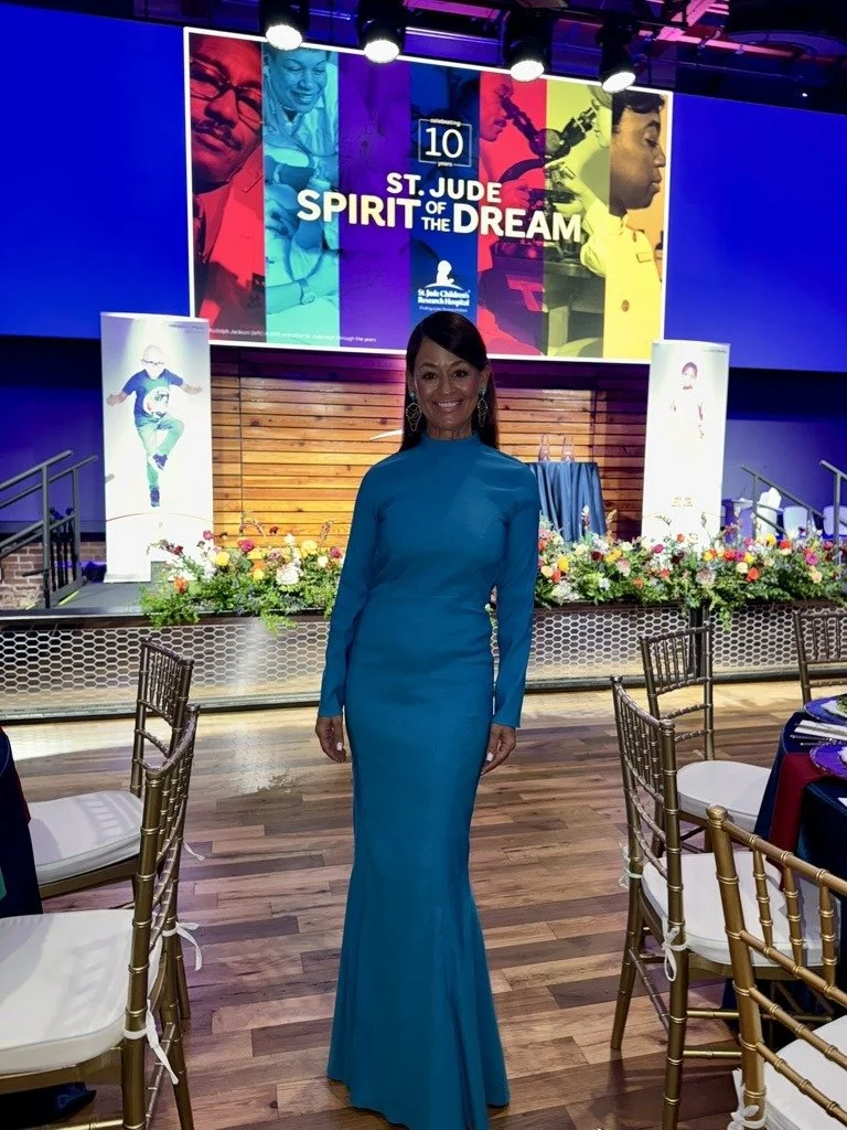 Yve Rojas in a long, bright blue dress standing in a decorated event hall with a stage and floral arrangements, celebrating the 10th anniversary of St. Jude Spirit of the Dream.