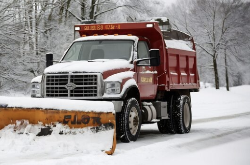 Red snow plow truck clearing snow on a snowy road.