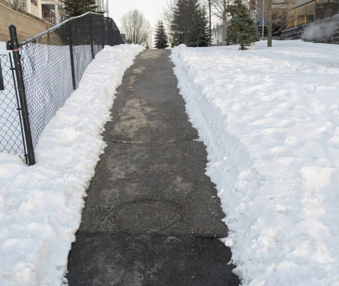 Snow-covered sidewalk with cleared path, black asphalt, on a cold winter day.