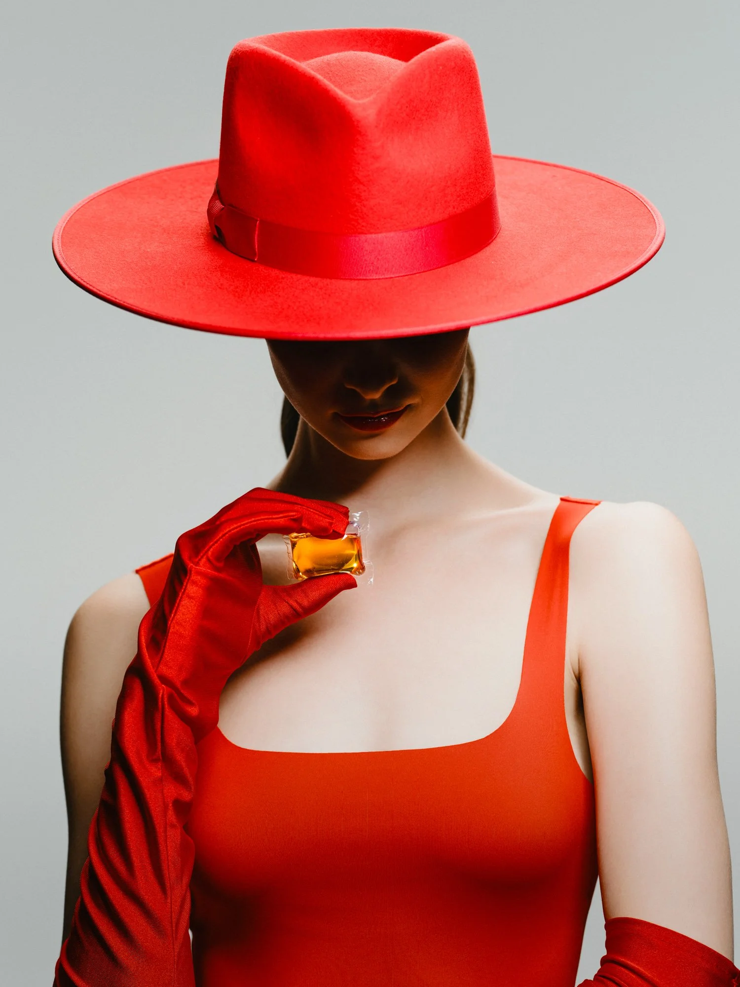 Woman wearing a large red hat with a wide brim, a red dress with thin straps, and red gloves, holding a small golden object.