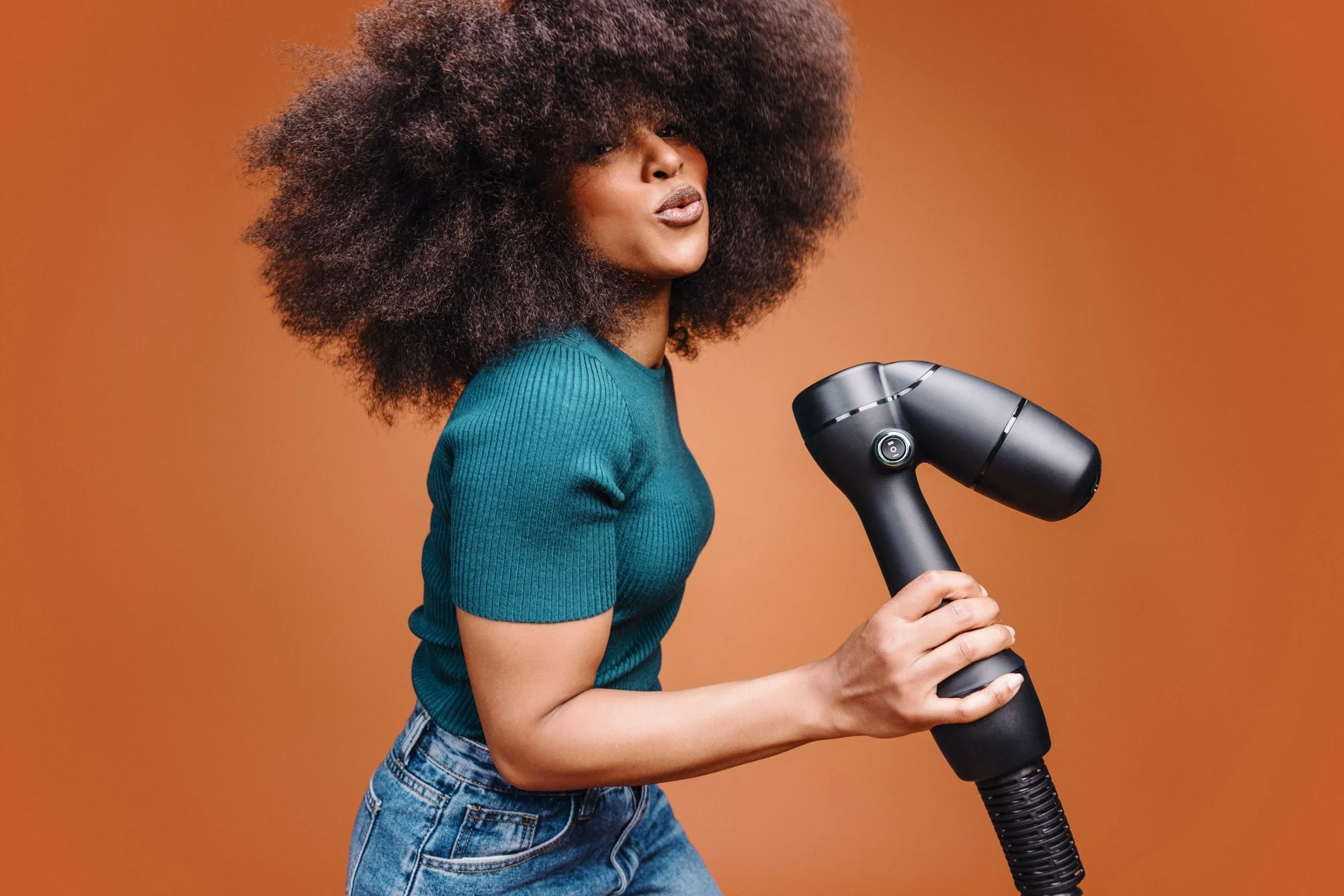 A woman with voluminous curly hair holding a black hairdryer.