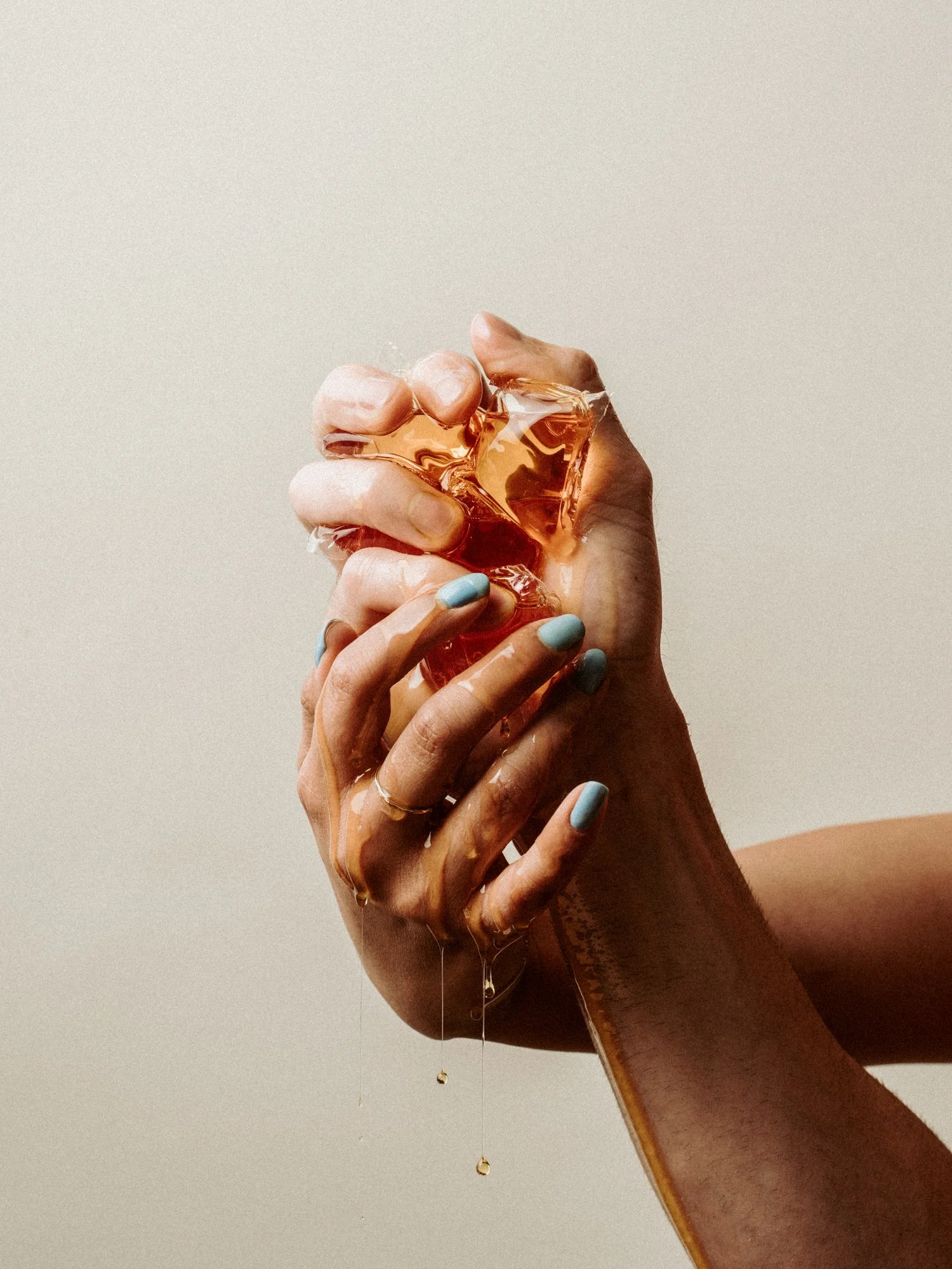 Hands holding a cracked glass gemstone with liquid dripping from it.