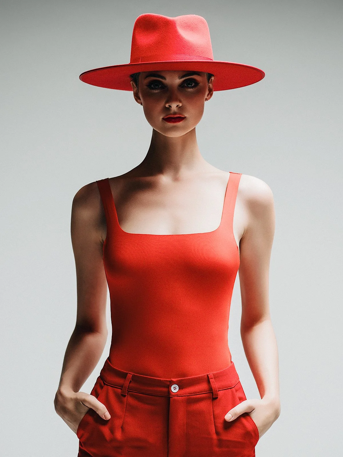 A woman wearing a red wide-brimmed hat, red sleeveless top, and red pants, standing against a plain light gray background.