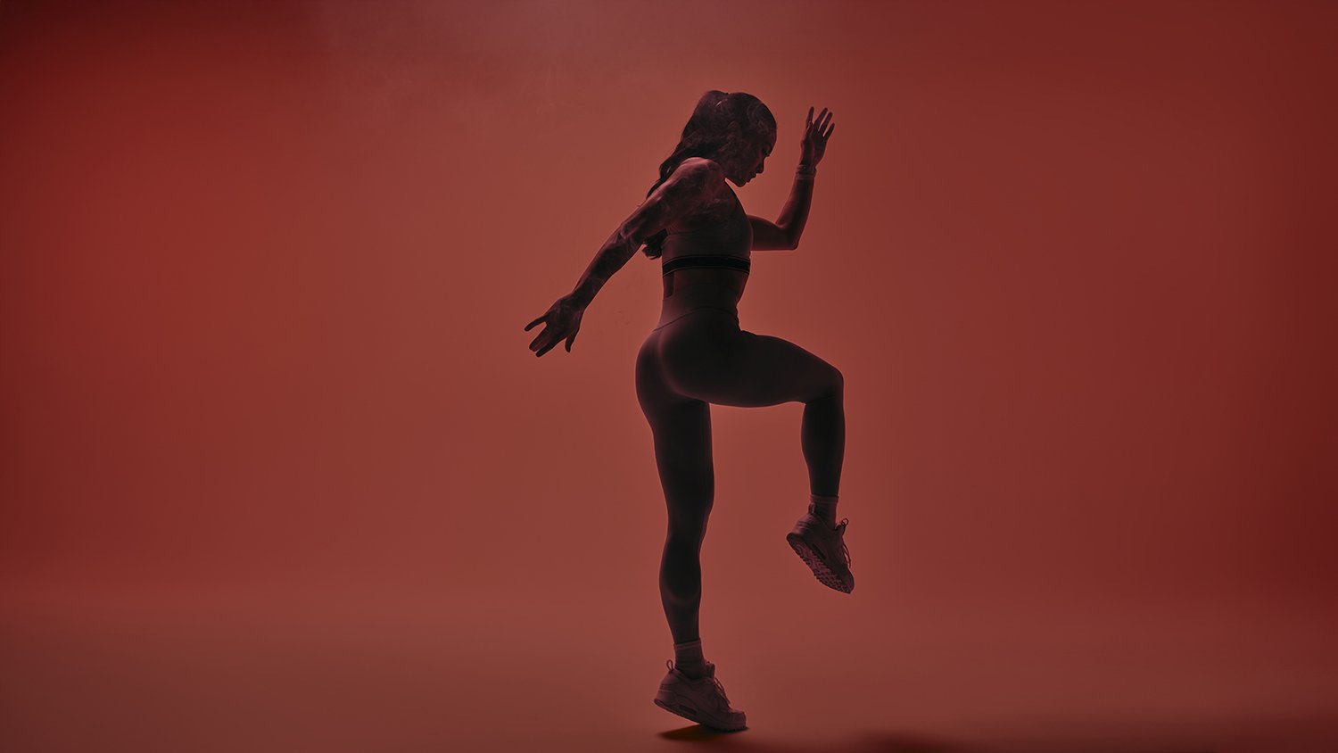 Silhouette of a woman in athletic clothing, balancing on one leg with the other raised, against a red background.
