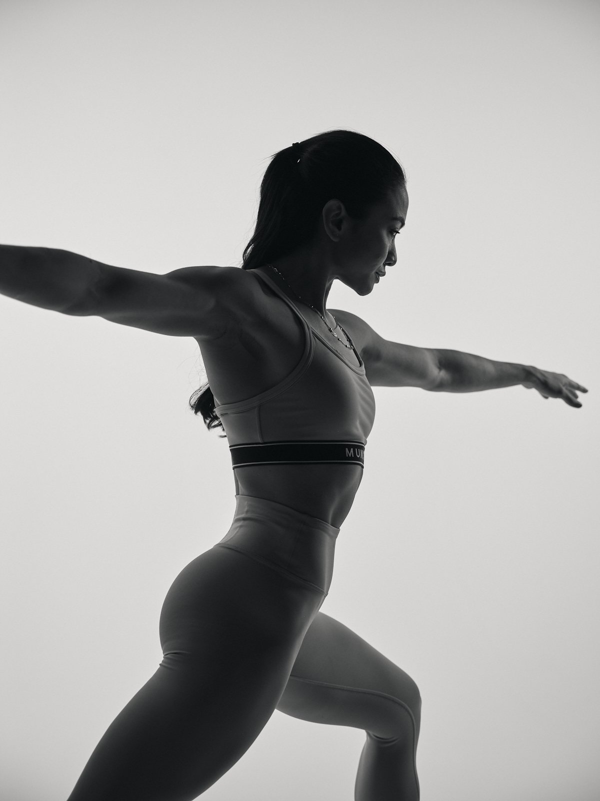 A woman in athletic wear performing a yoga pose with arms outstretched on a plain background.