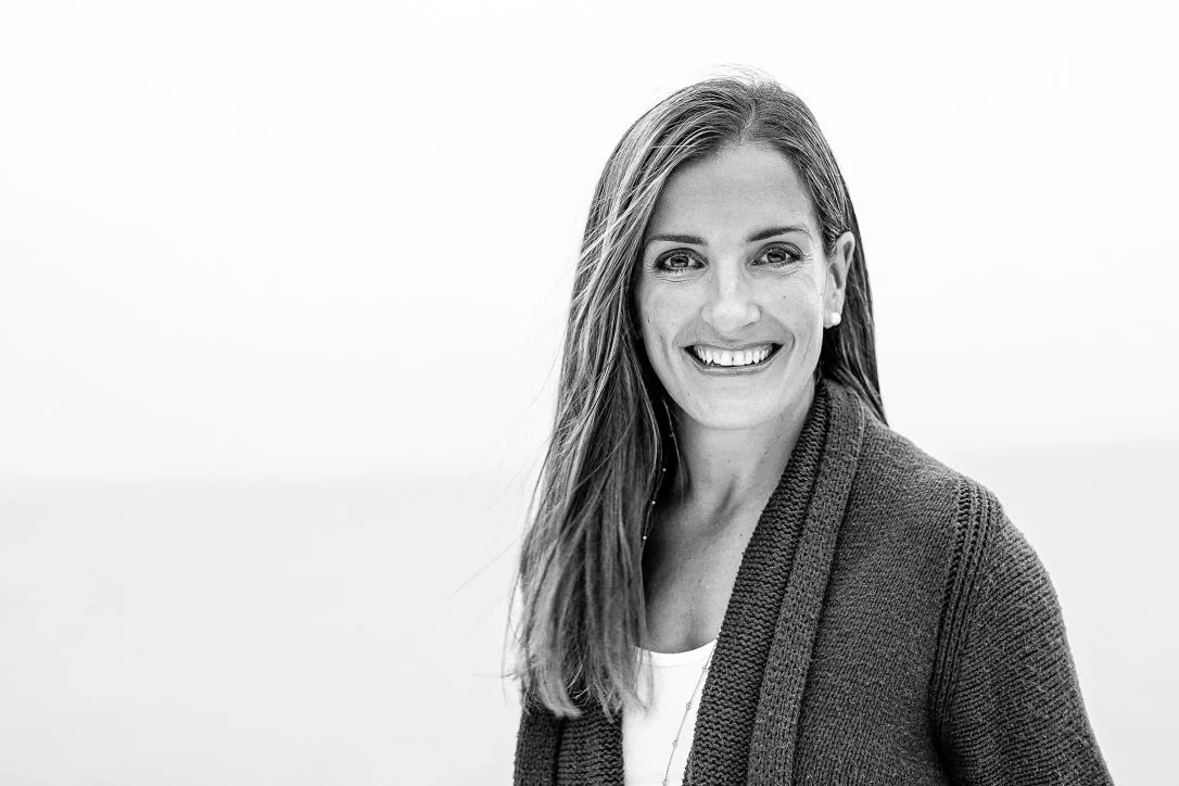 Black-and-white portrait of a smiling woman with long hair, wearing a dark cardigan and light top, against a plain background.