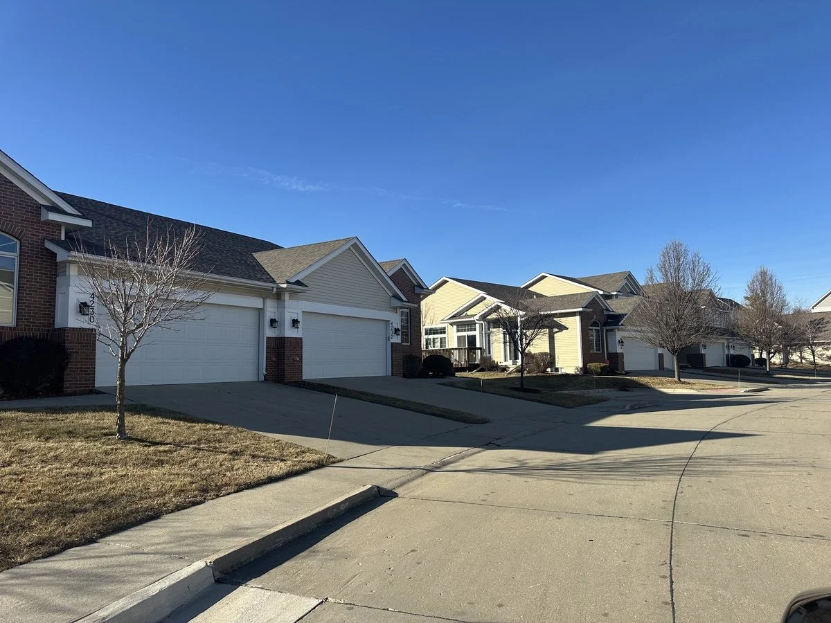 Row of suburban houses with driveways and leafless trees under a clear blue sky.