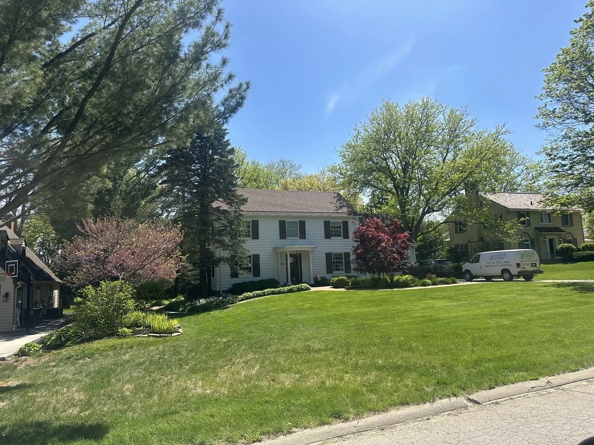 A residential neighborhood with green lawns, trees, and houses under a blue sky.