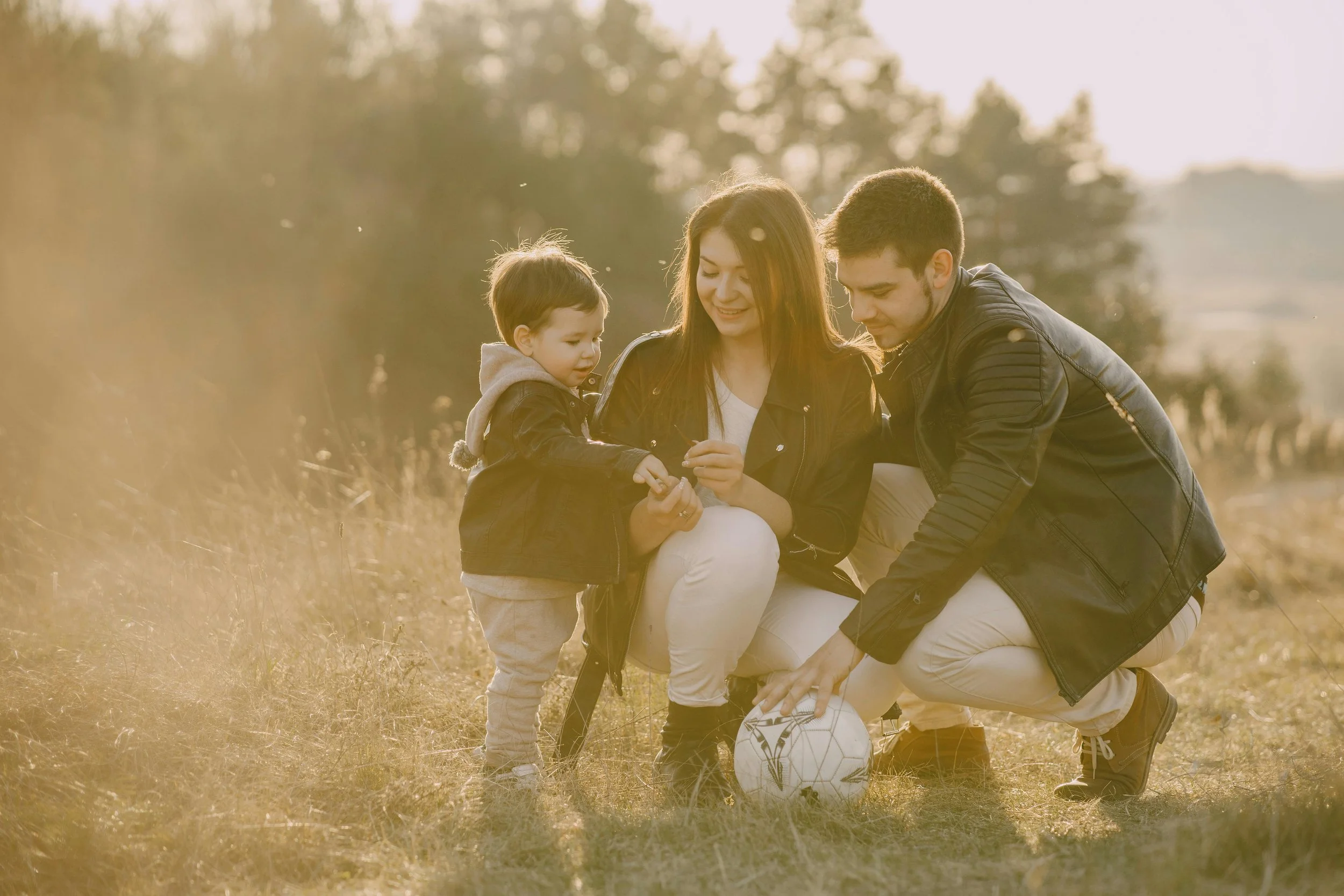 Una familia jugando con un balón en un campo al atardecer.