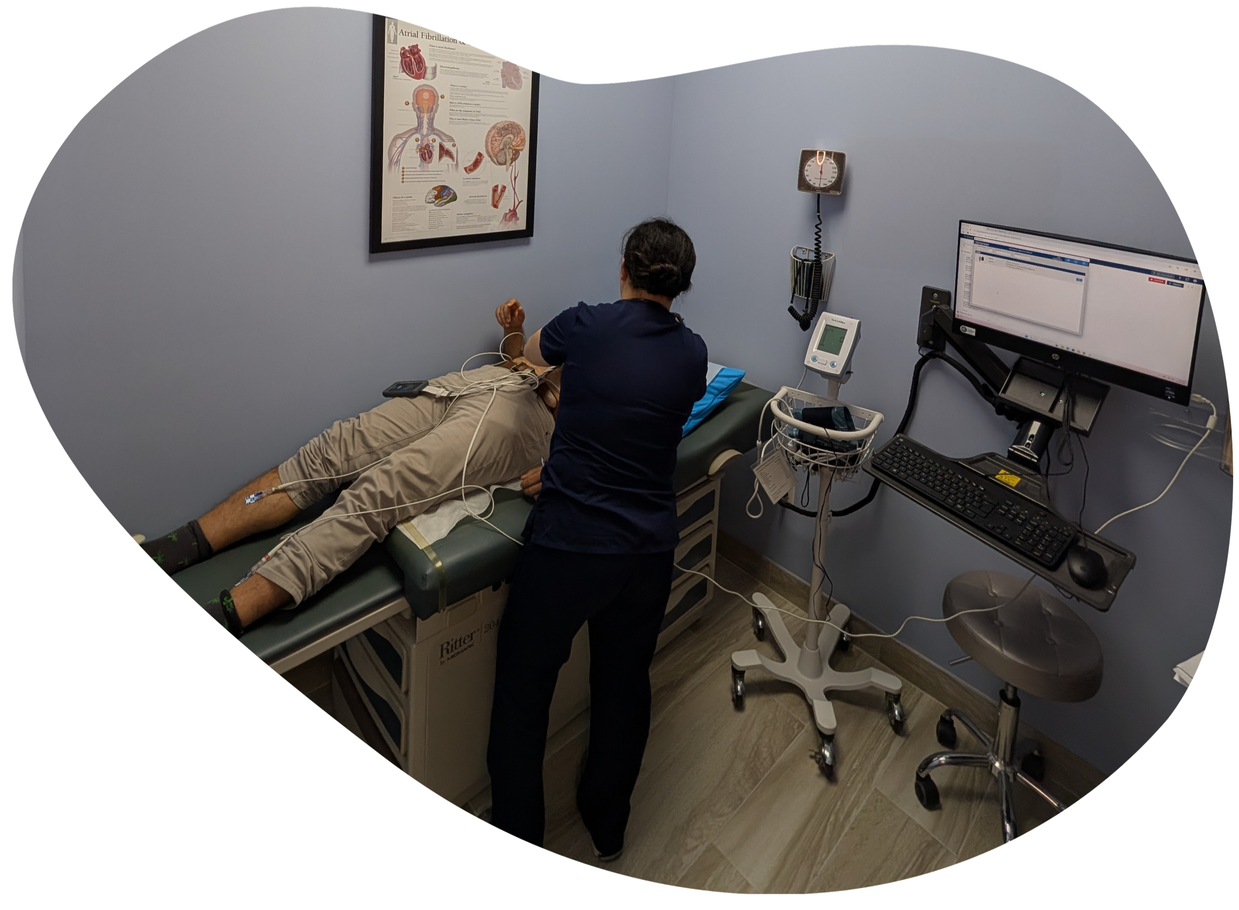 Primary care provider performing a medical examination on a patient in a clinical exam room with monitoring equipment.