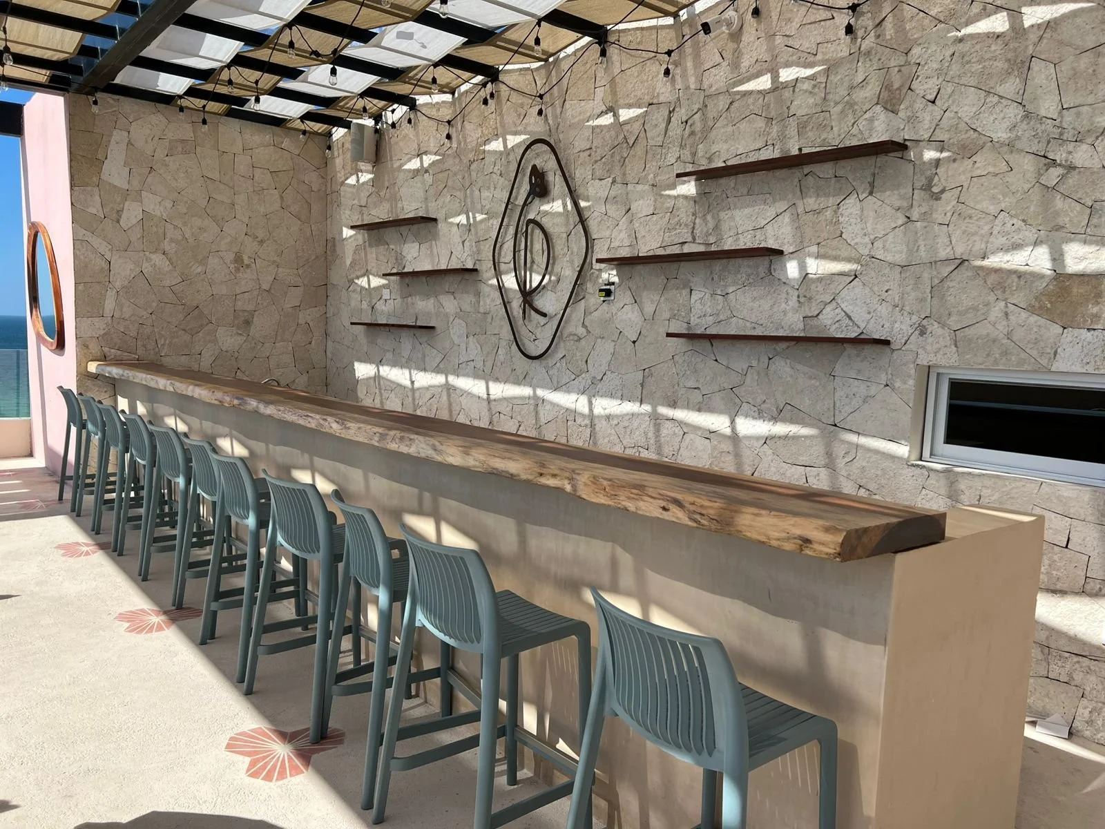 Bar de verano con estación de servicio y sillas de plástico junto a pared de piedra y decoración moderna.